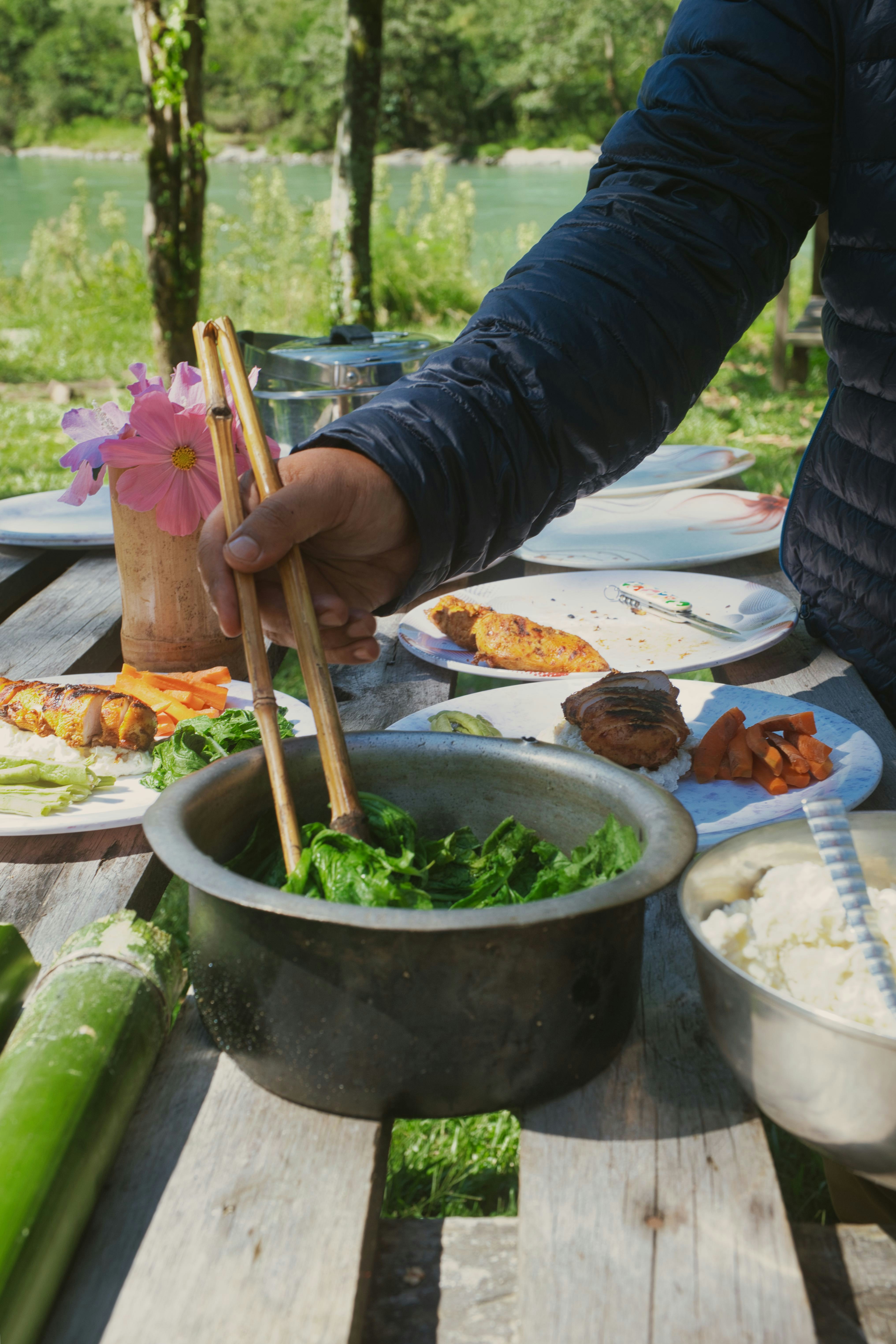 Person serving food at an outdoor picnic table.