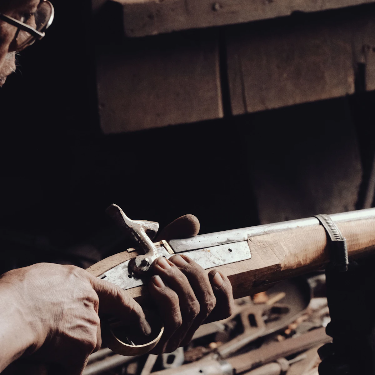 Manos de un armero ajustando el mecanismo de un rifle antiguo en su taller.