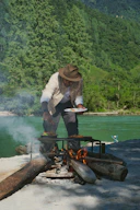Man cooking food over a campfire by a river