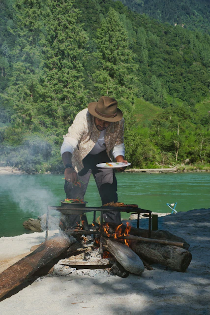 Man cooking food over a campfire by a river