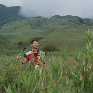 Man in traditional attire in a grassy mountain landscape