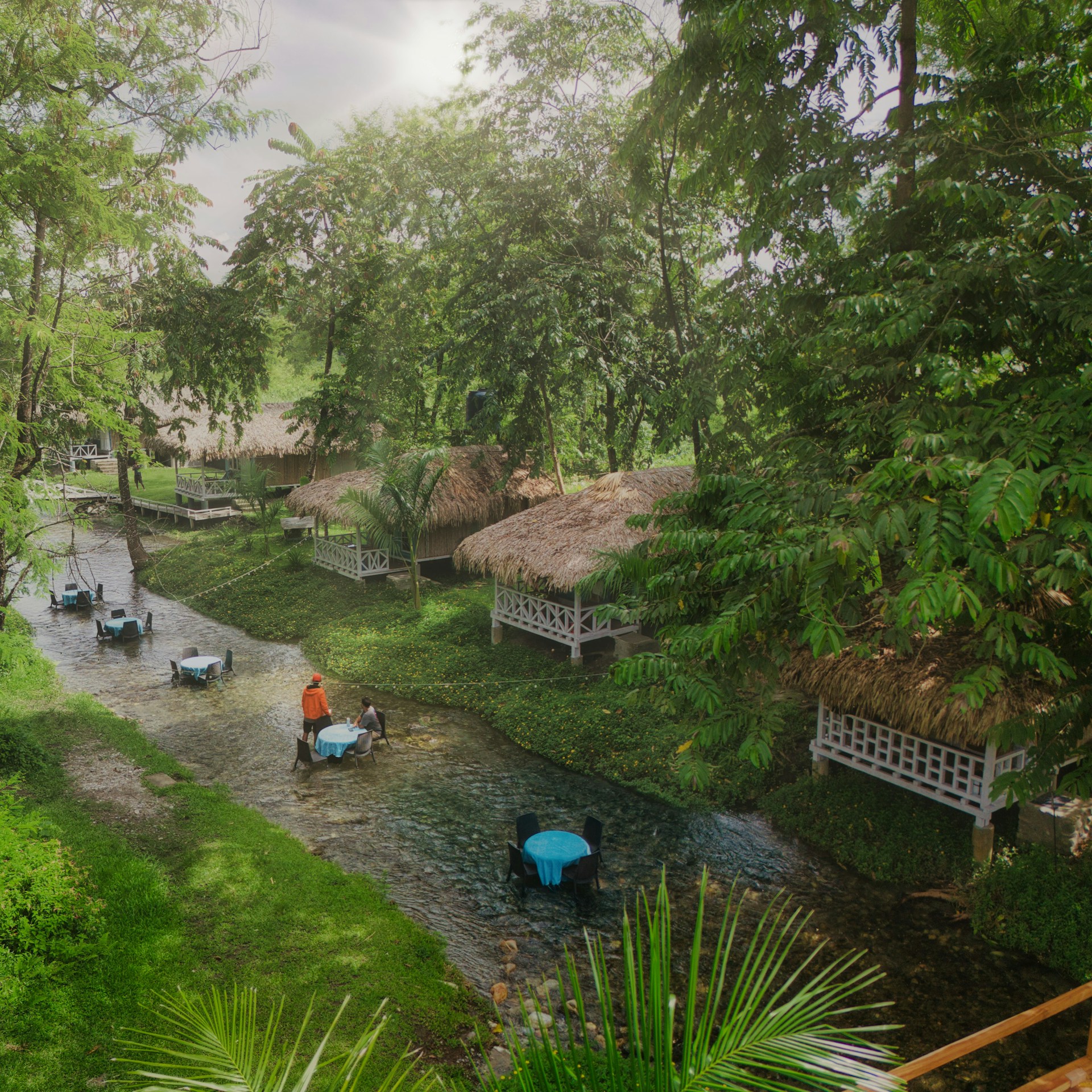 Tropical resort with huts and tables in stream.