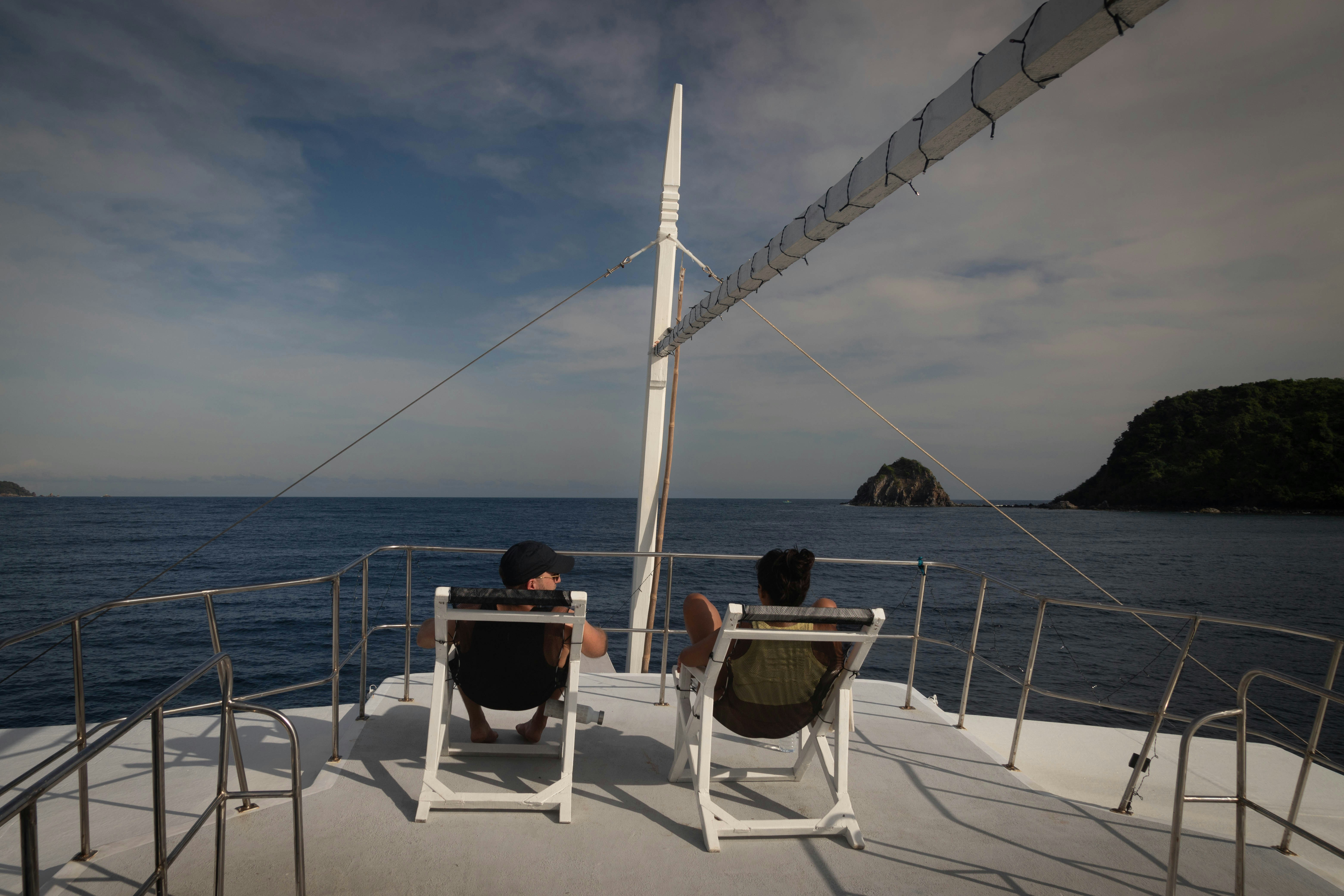 Two people relax on a boat deck overlooking the ocean.