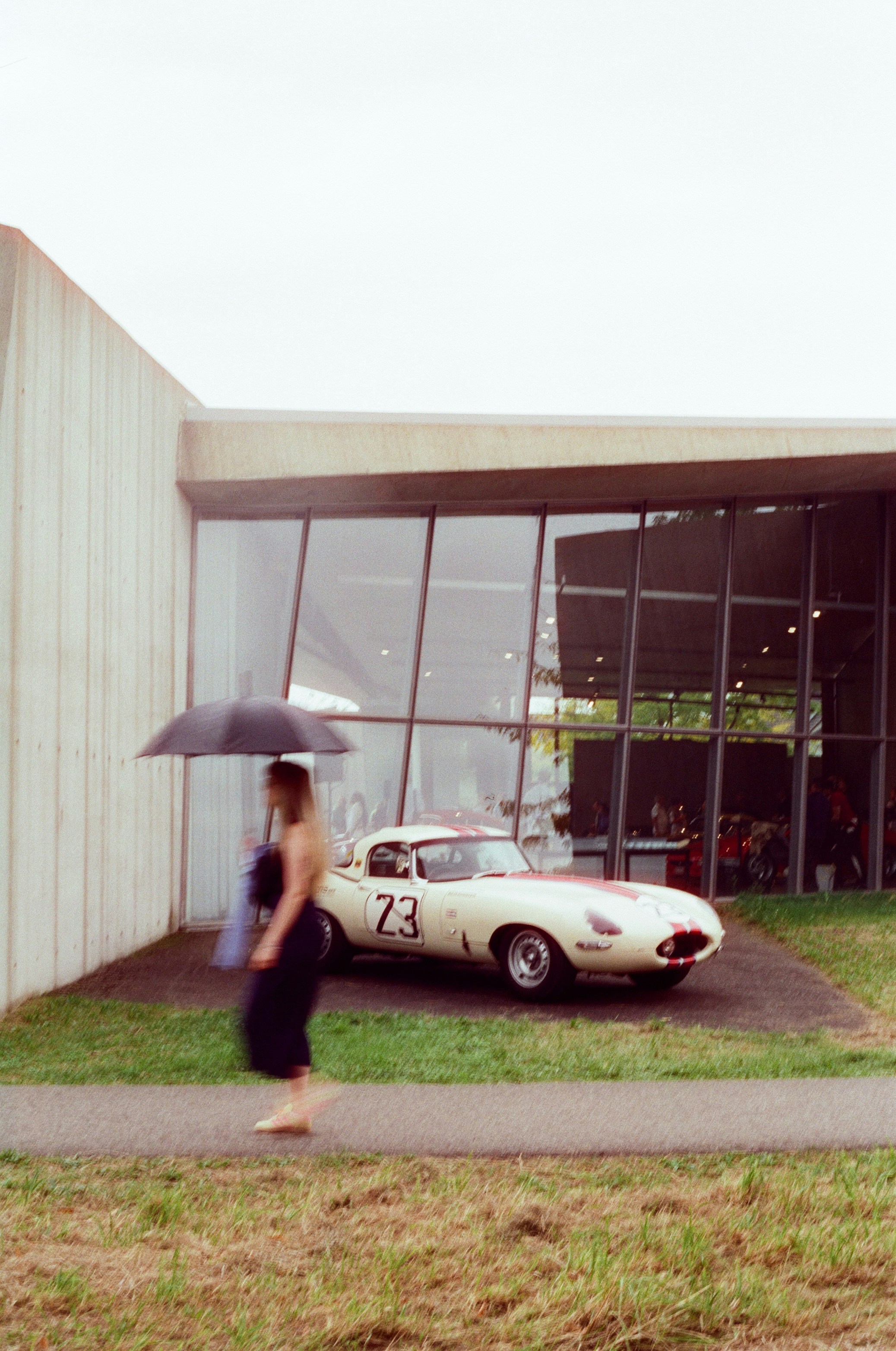 Woman with umbrella walks past vintage car.