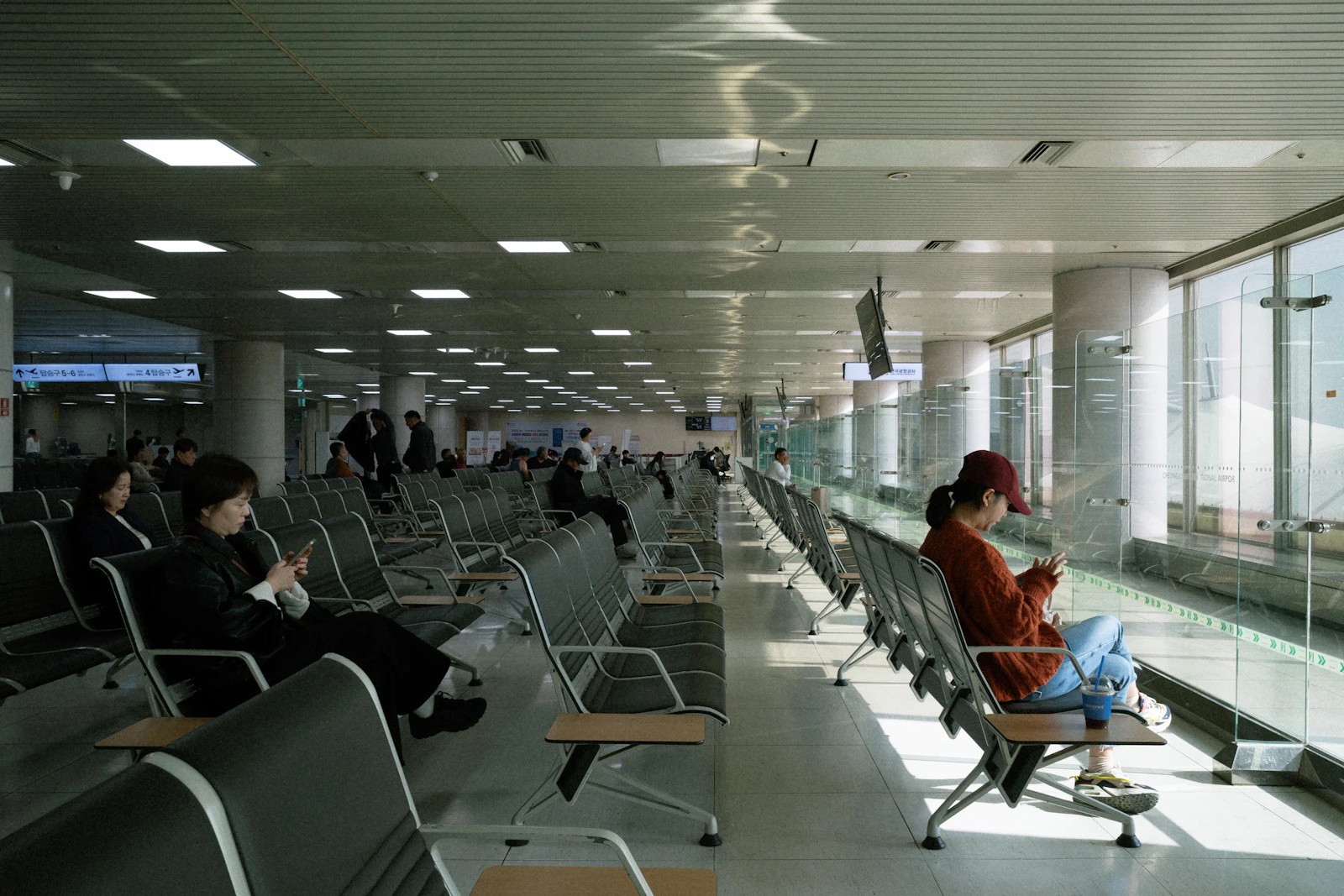 Travelers seated in a bright modern airport lounge beside large windows
