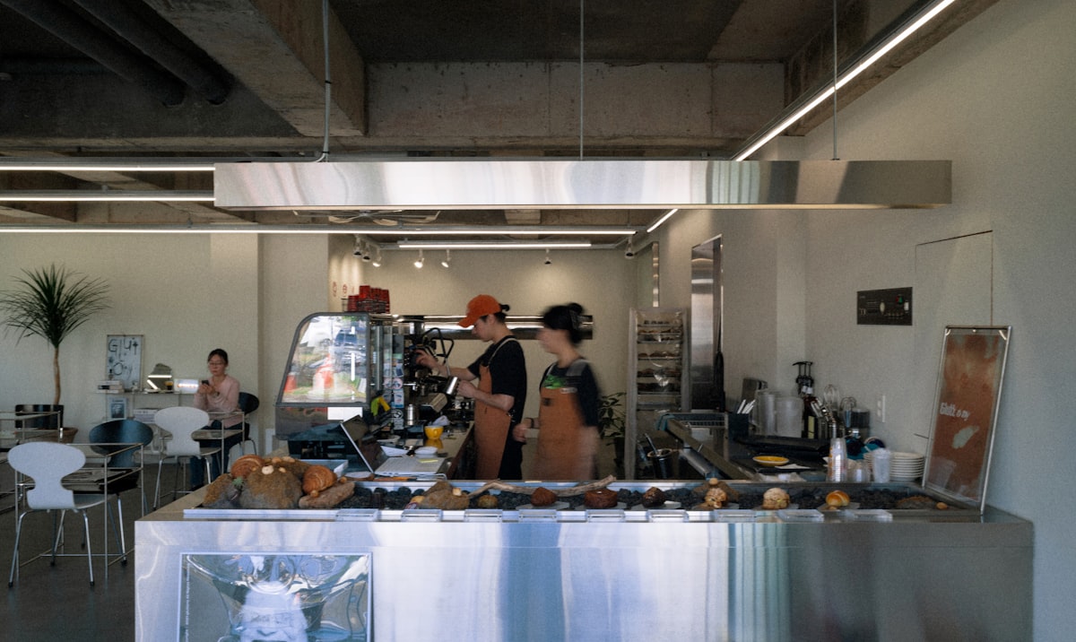 Baristas preparing drinks behind a modern cafe counter with pastry display