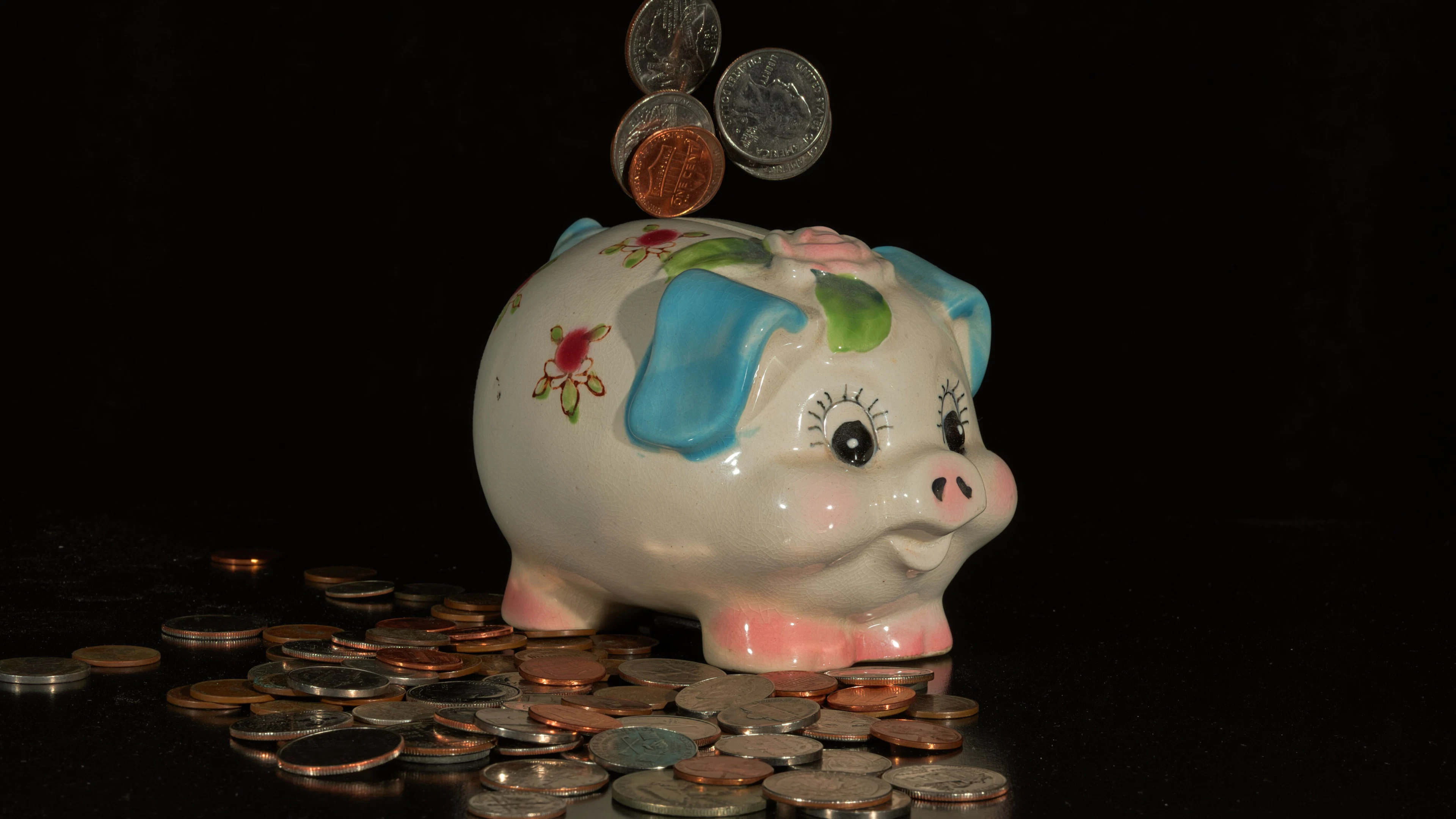 Coins dropping into a painted ceramic piggy bank on a black background