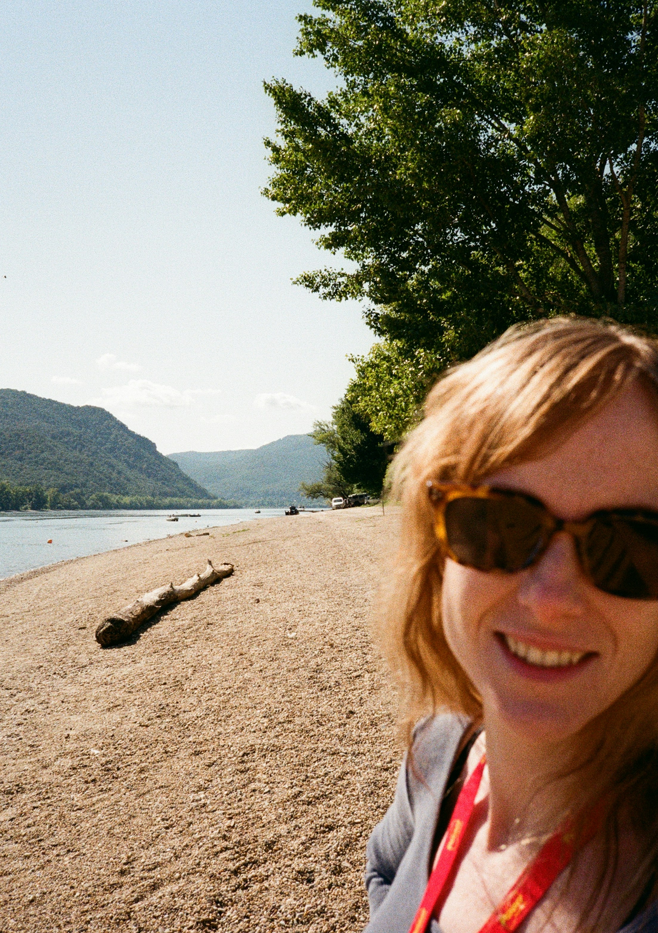 Woman smiling on a sandy beach with mountains.
