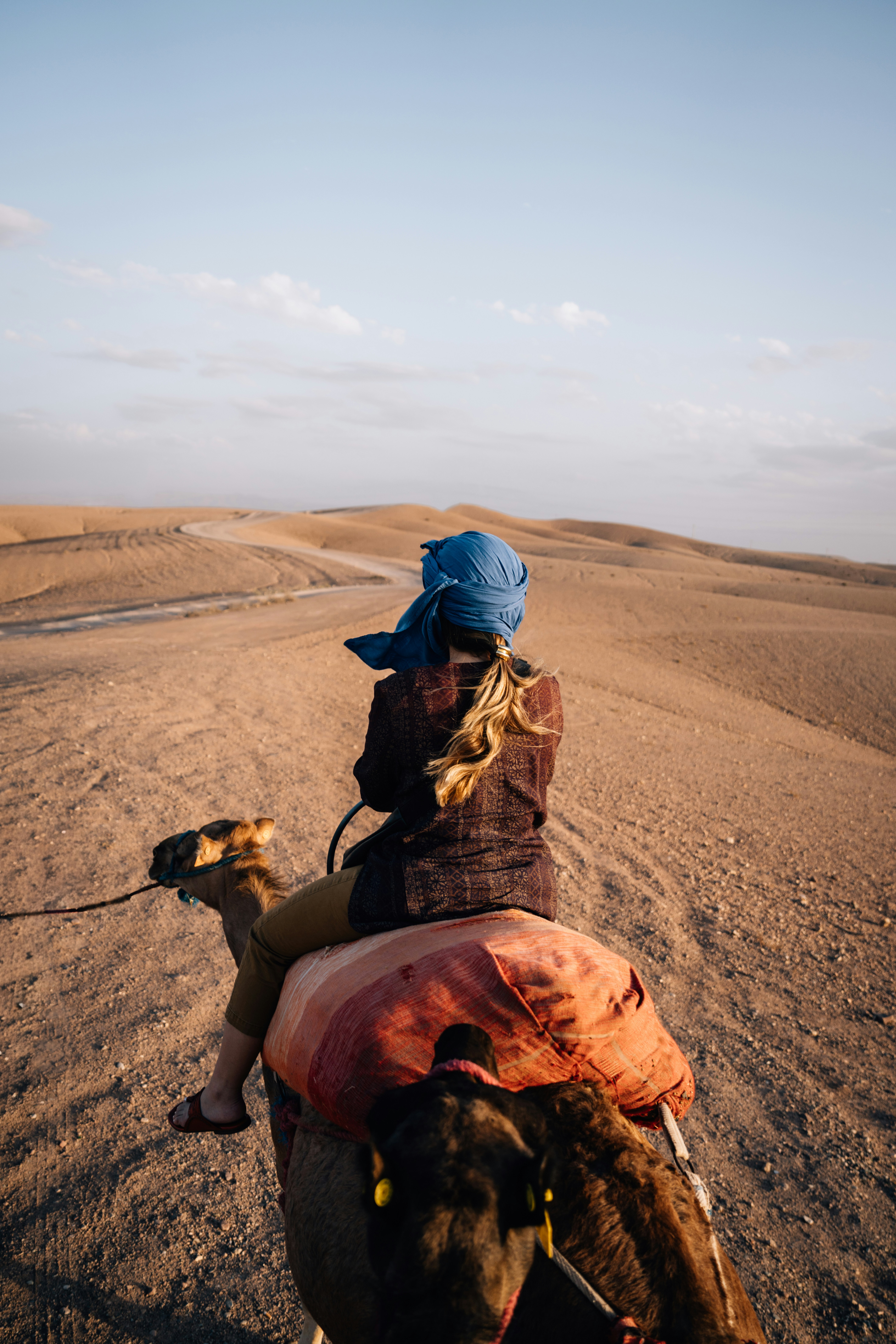 Personne chevauchant un chameau à travers les dunes du désert au coucher du soleil.