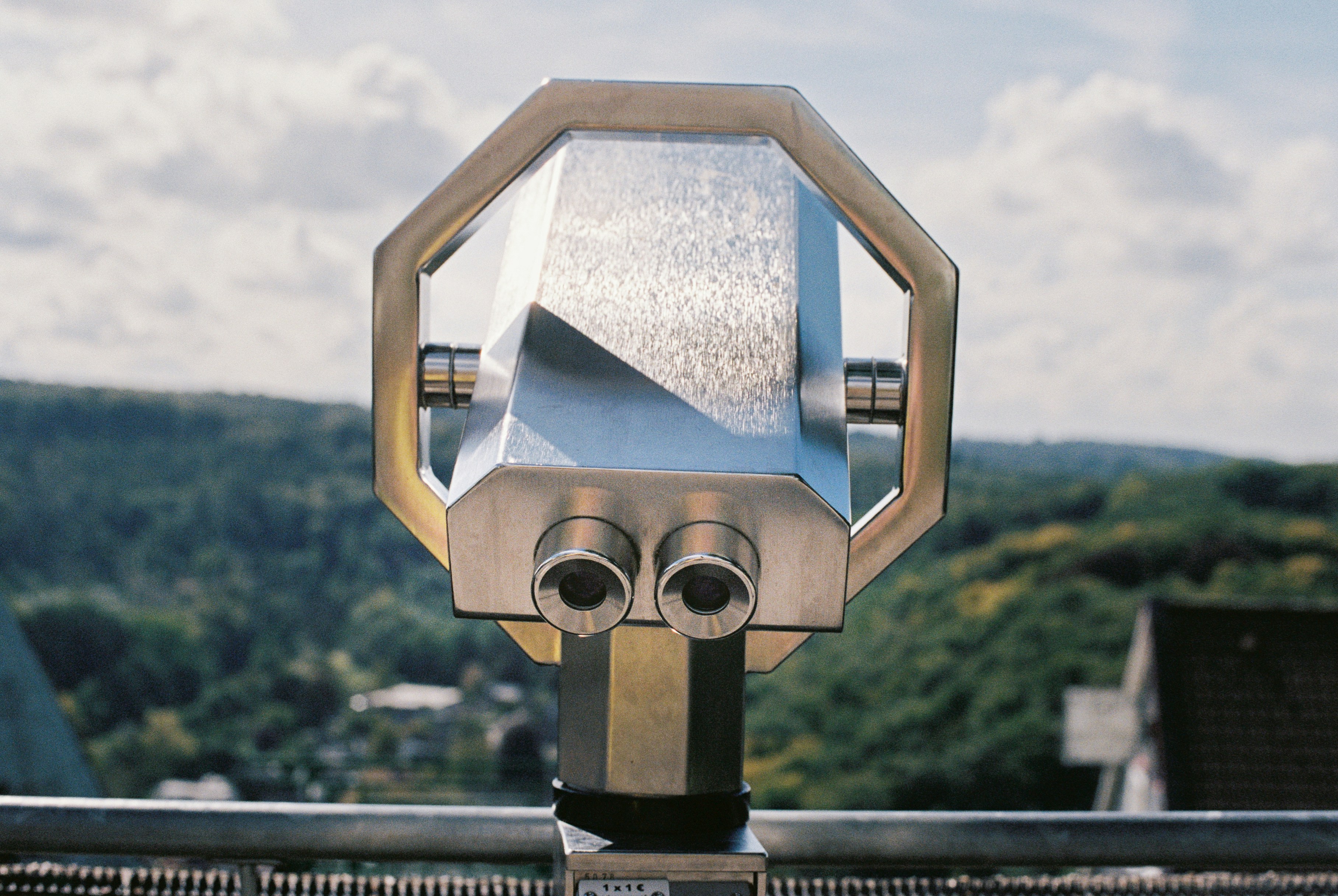Tourist binoculars observation deck analog photography. Stainless steel viewfinder on scenic viewpoint overlooking forested hills, captured on vintage film with shallow depth of field