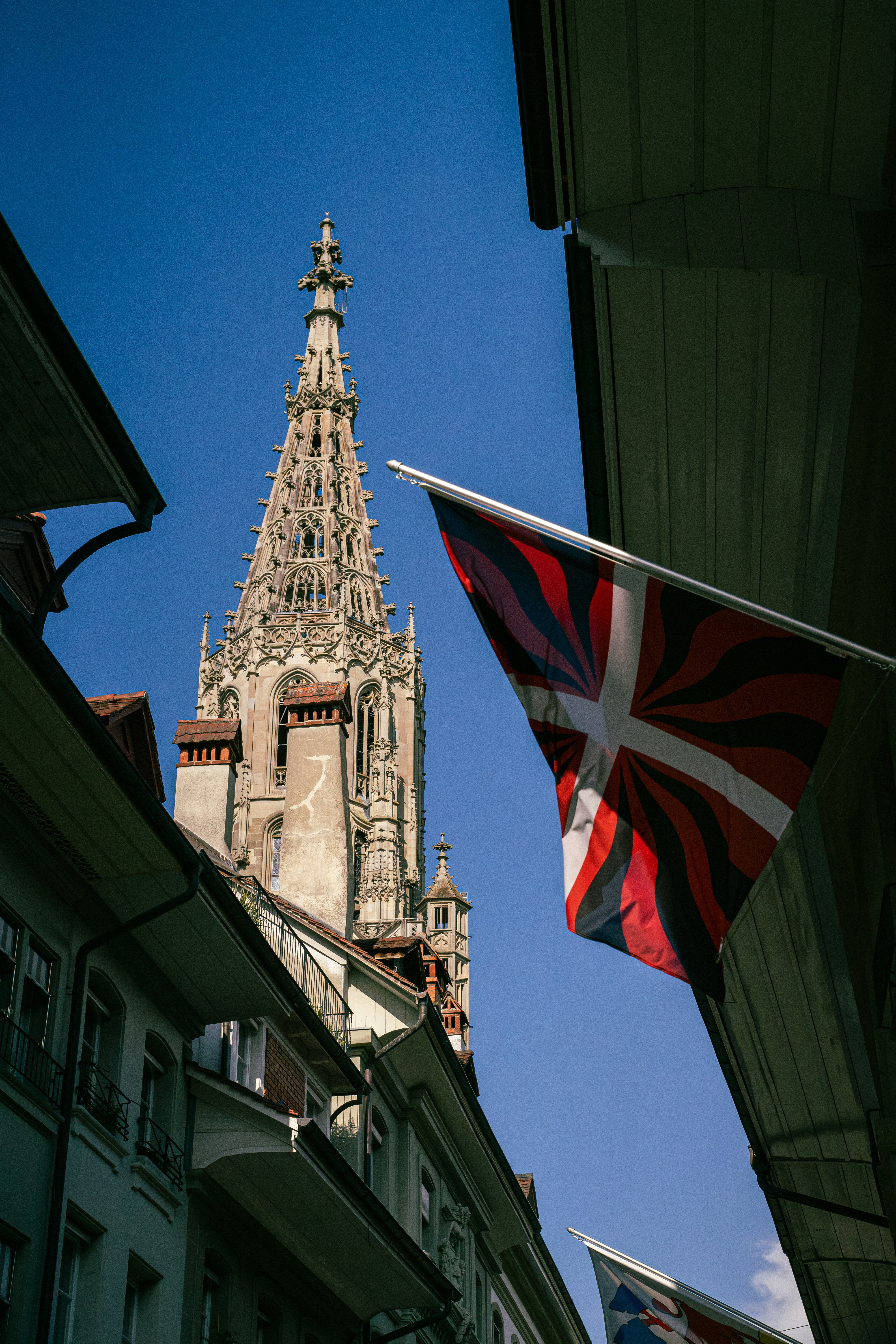 Gothic cathedral spire with flags against blue sky.