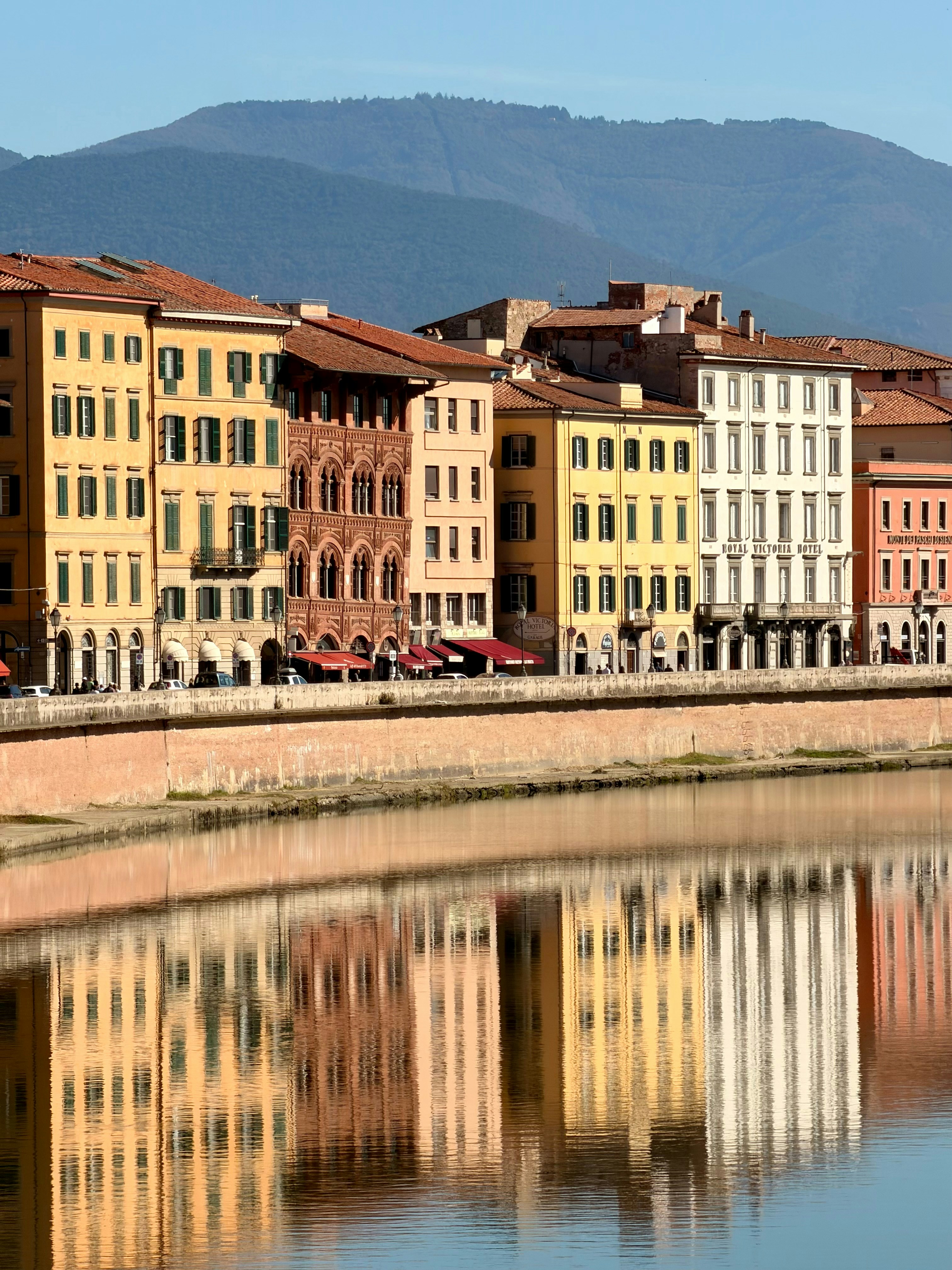 Colorful buildings line a river with reflections.