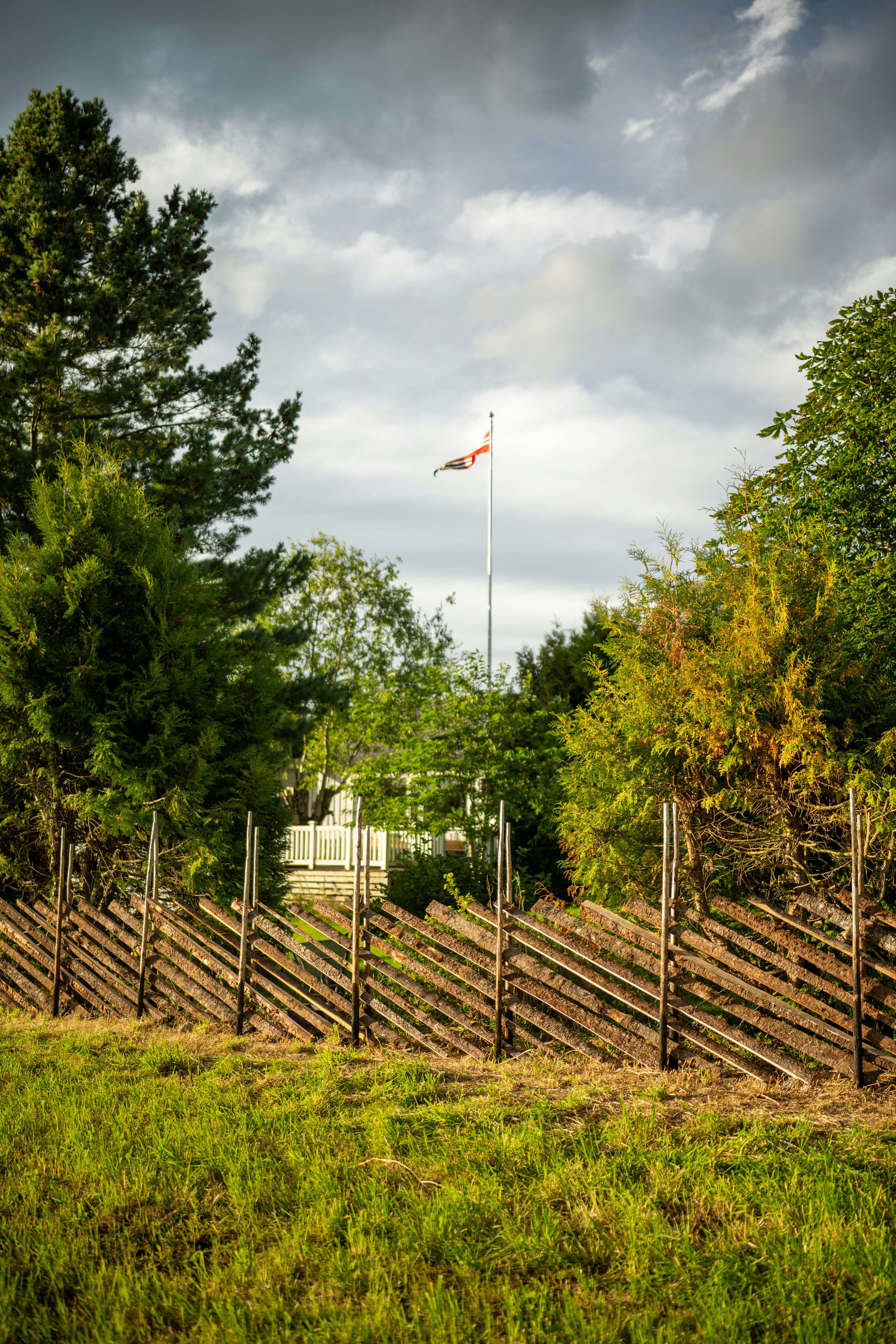 Wooden fence with flag and trees under cloudy sky