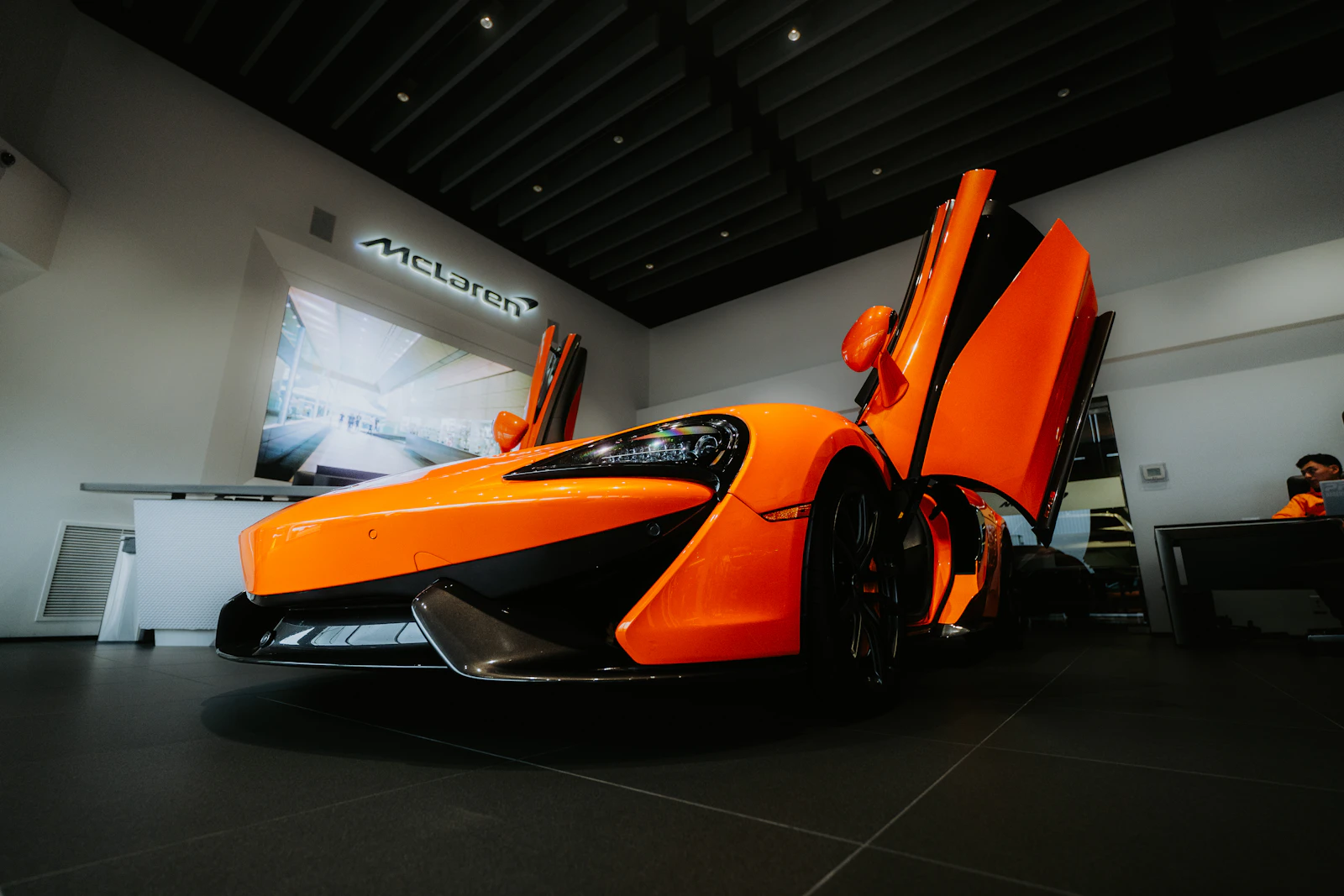 Orange McLaren with doors up inside a McLaren showroom
