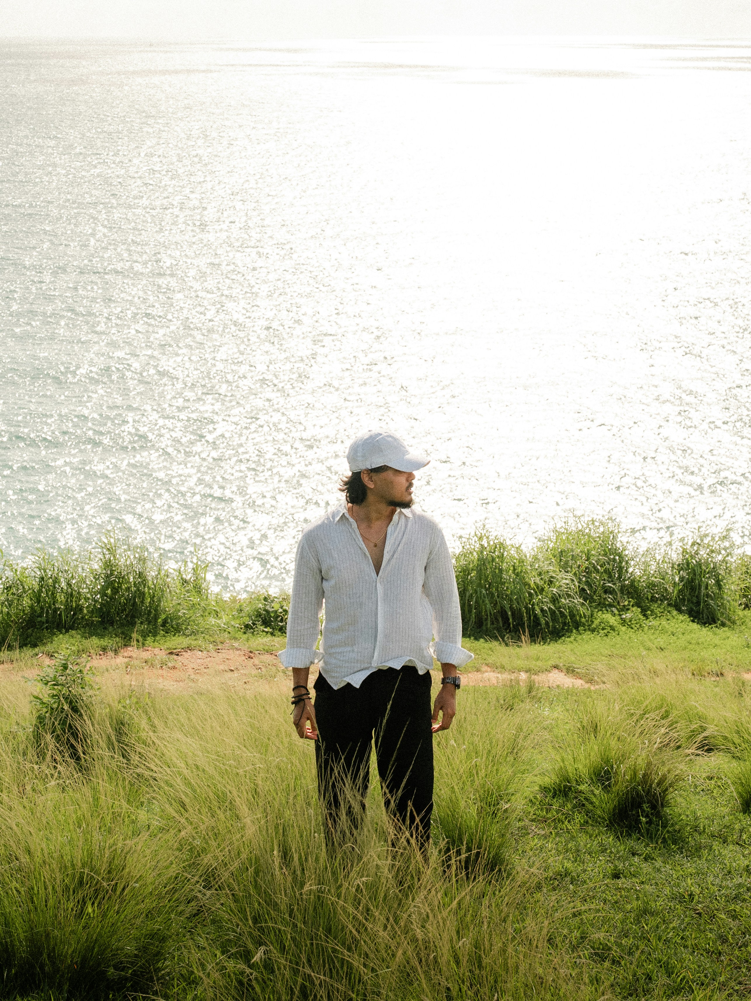 Man in white shirt and cap by the ocean