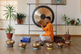 Man playing a large gong with singing bowls around him
