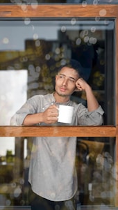 A man holding a mug looking out a window