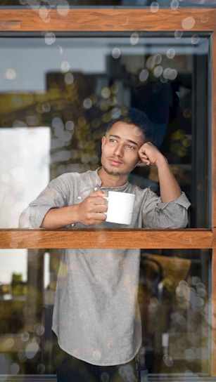 A man holding a mug looking out a window