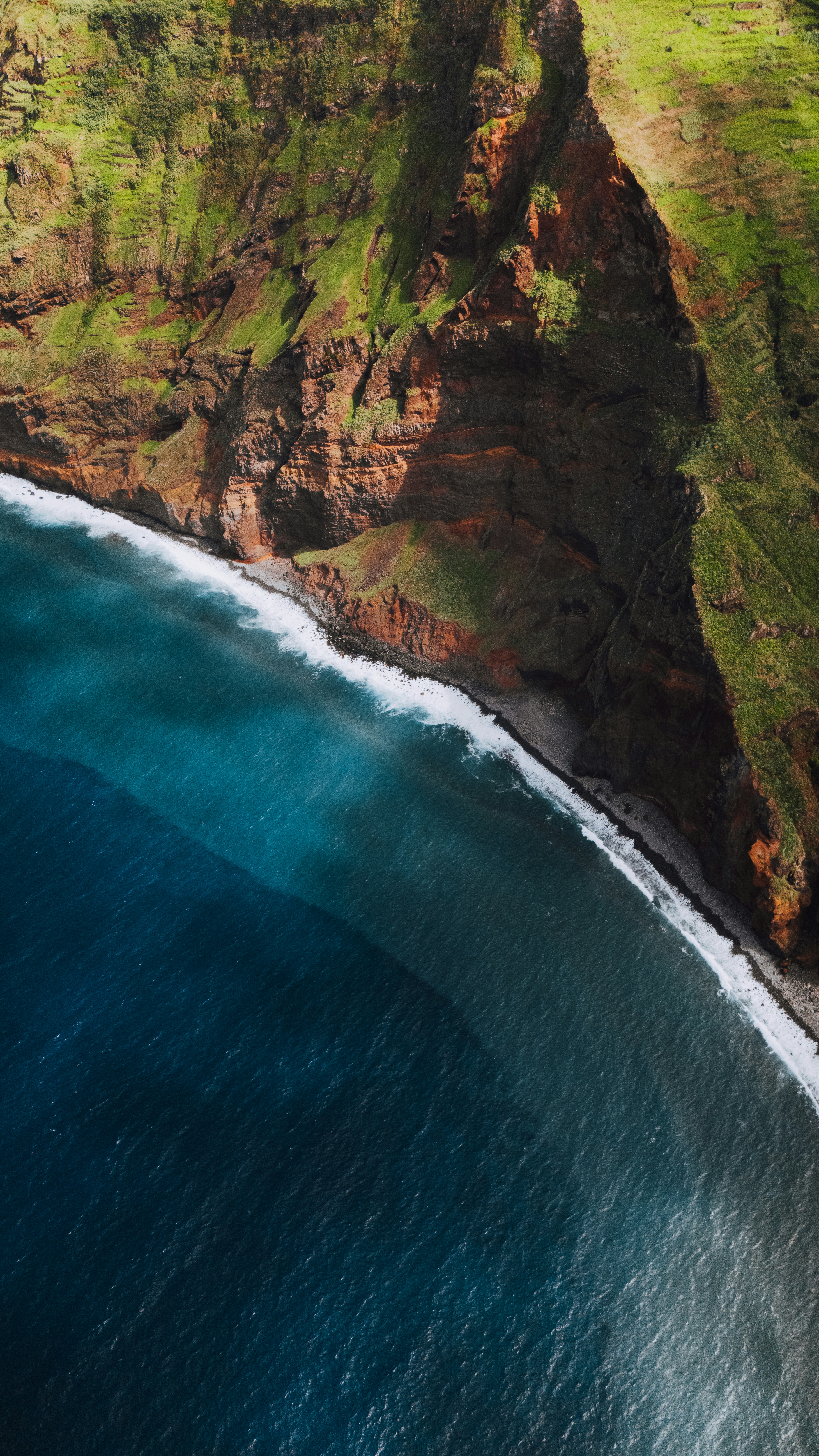 Rugged green cliffs meet the deep blue ocean waves.