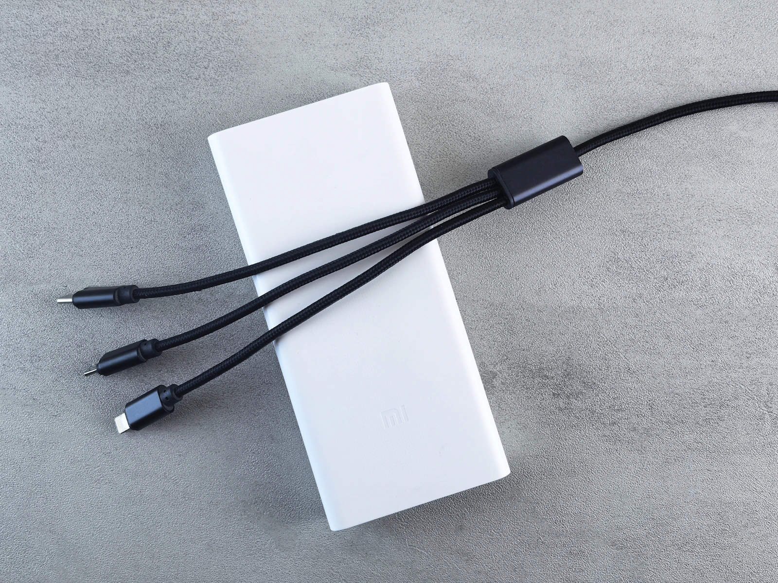 White portable power bank with three charging cables arranged on a neutral surface