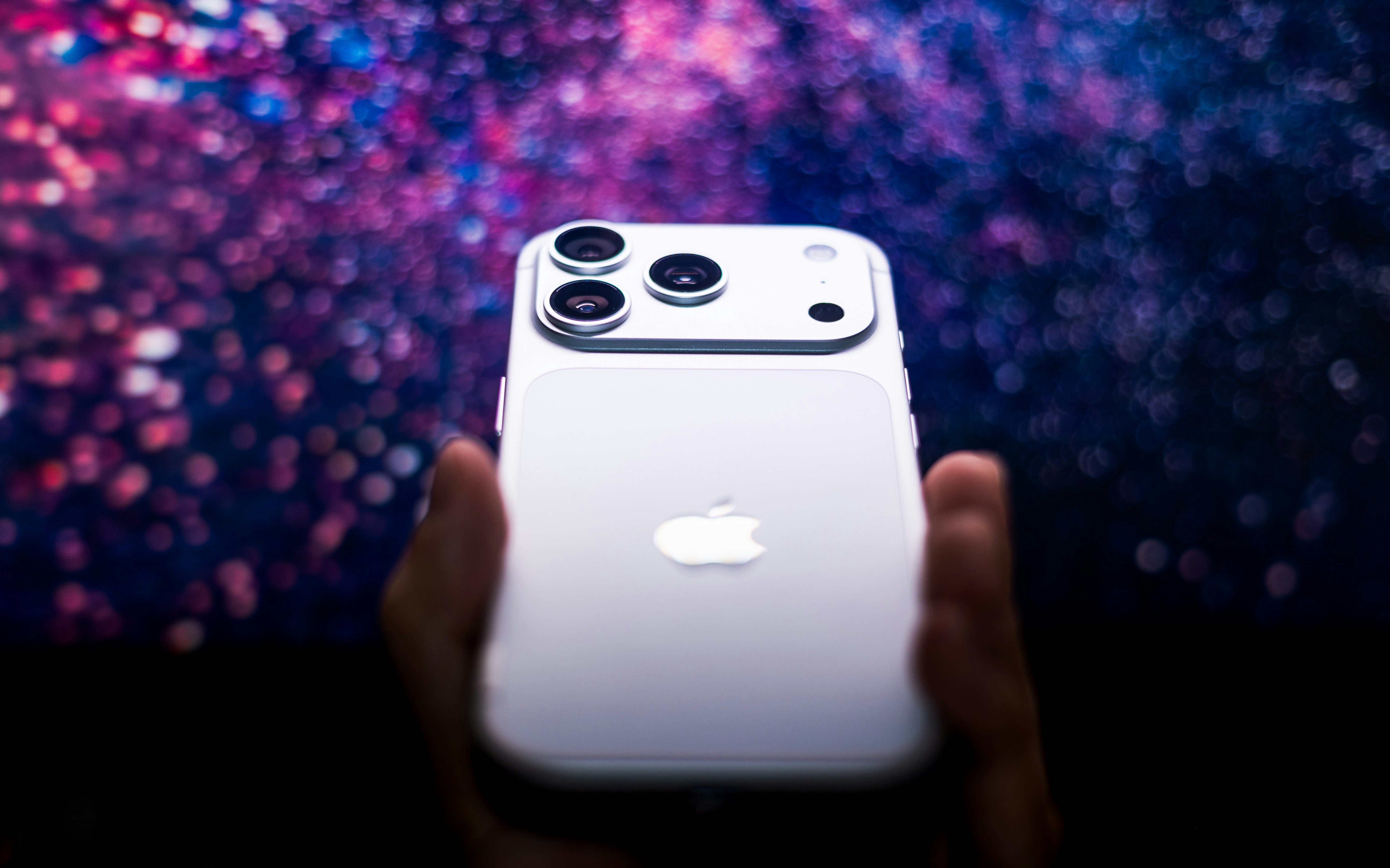 カラフルなボケ味の背景を持つ白いiPhoneを手に持つ