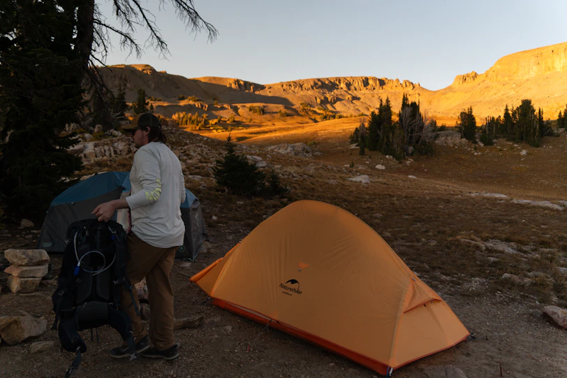 Campers setting up tent at sunrise with mountain backdrop
