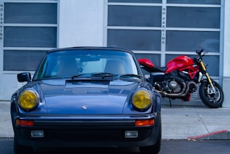 Blue vintage car and red motorcycle parked outside.