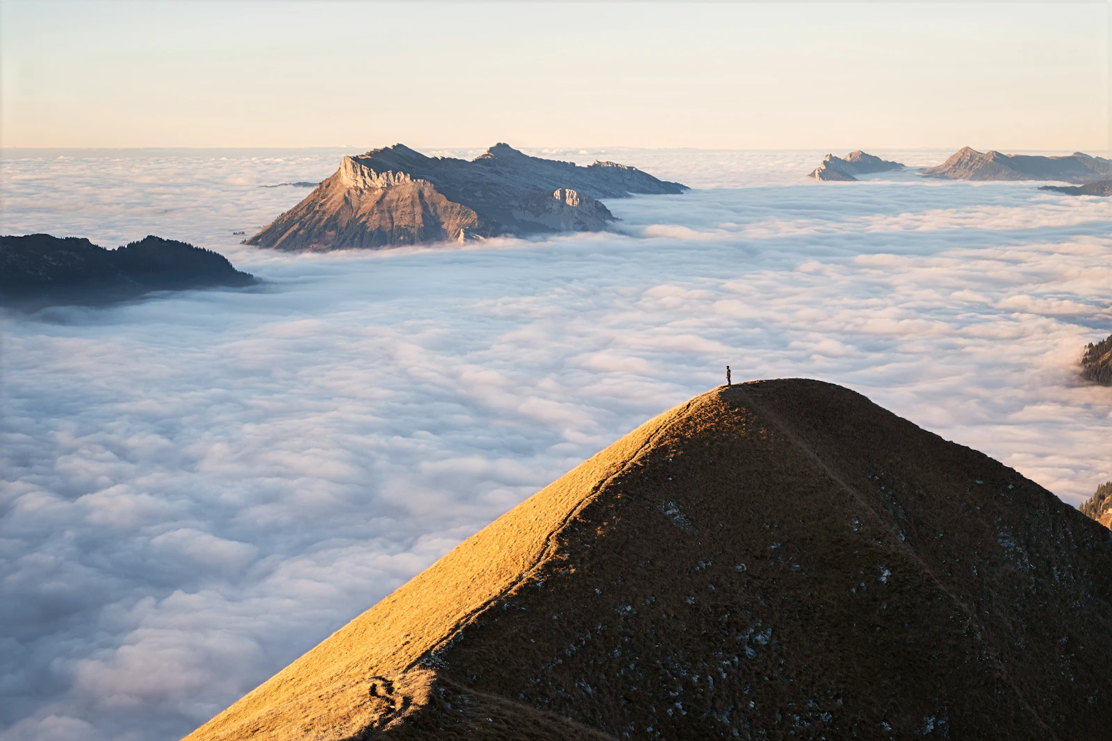 A lone hiker standing on a mountain peak above the clouds