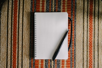 A blank notebook with a pen on striped fabric.