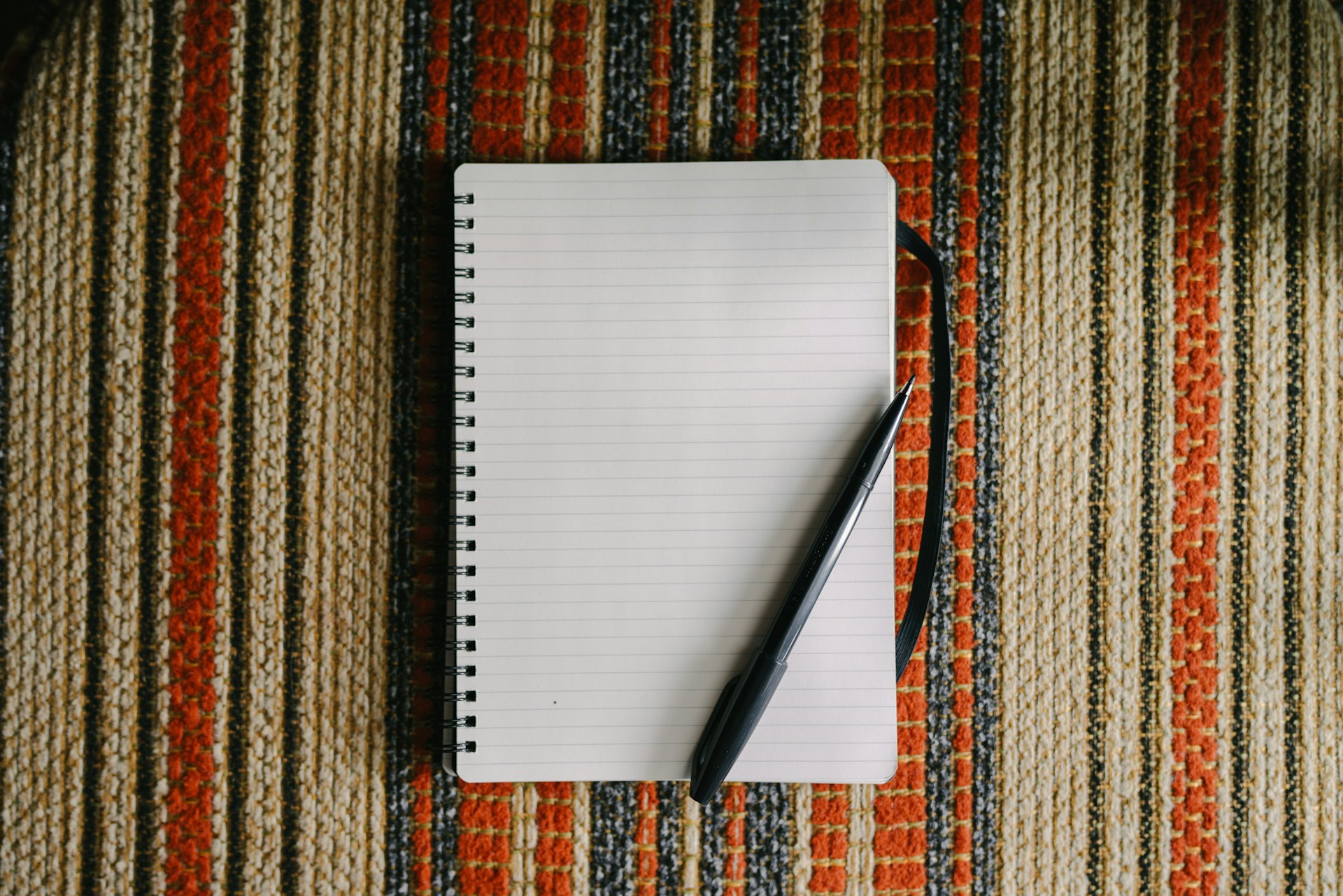 A blank notebook with a pen on striped fabric.