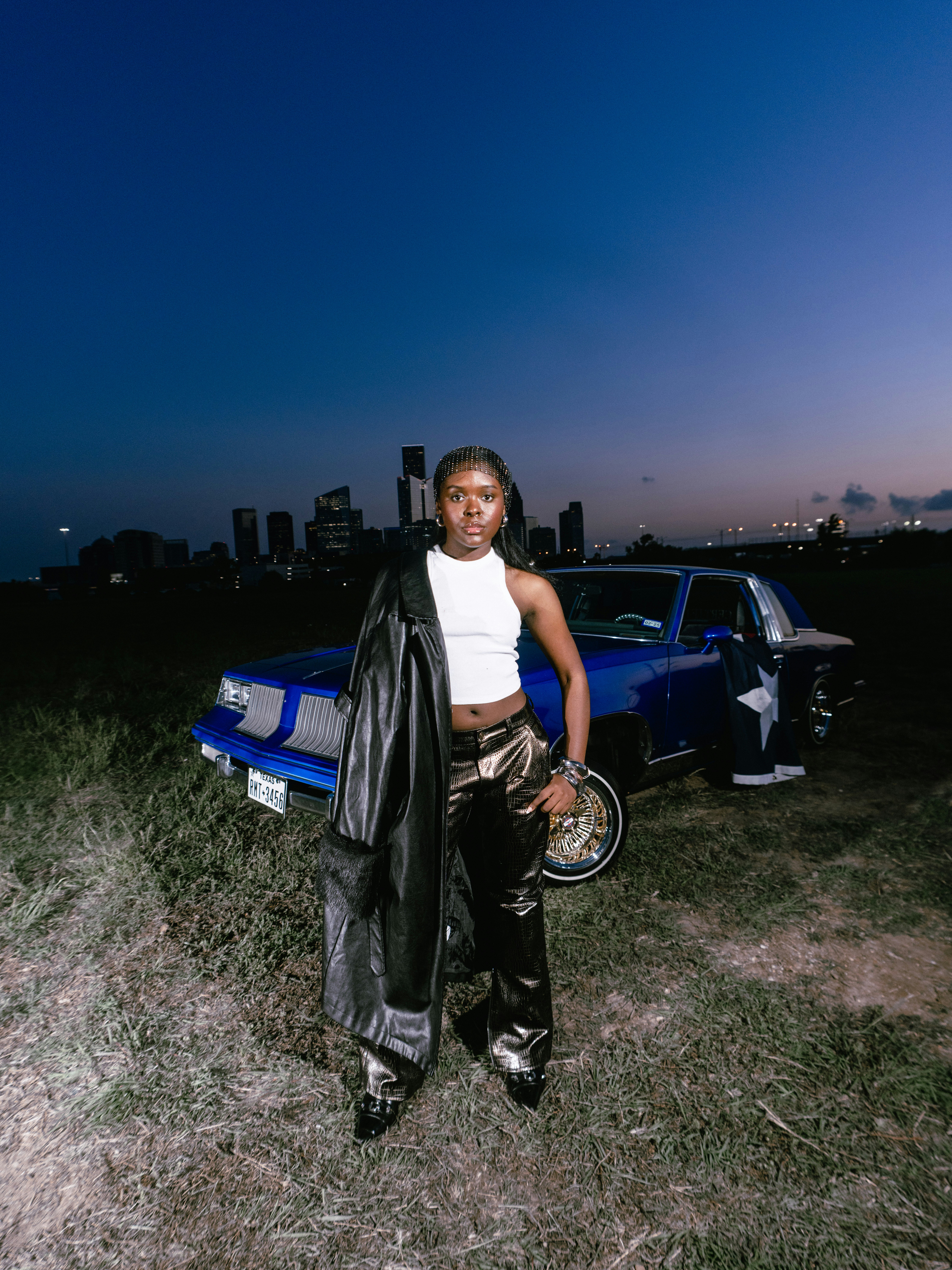 Woman in shiny pants with a classic car at dusk