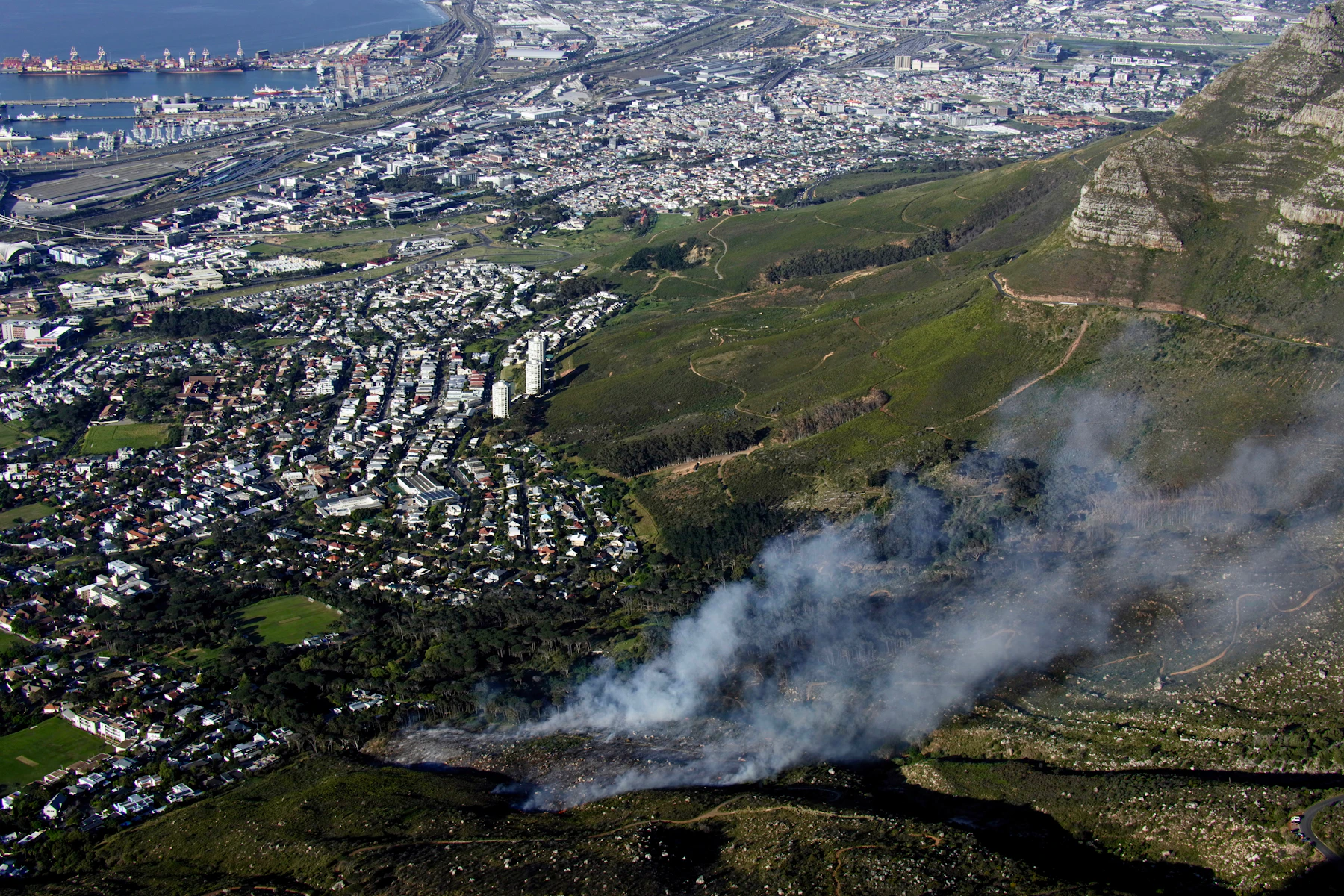 Wildfire smoke plume rising from a mountainside above a populated valley