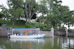 Boat docked on a calm lake with trees and building.