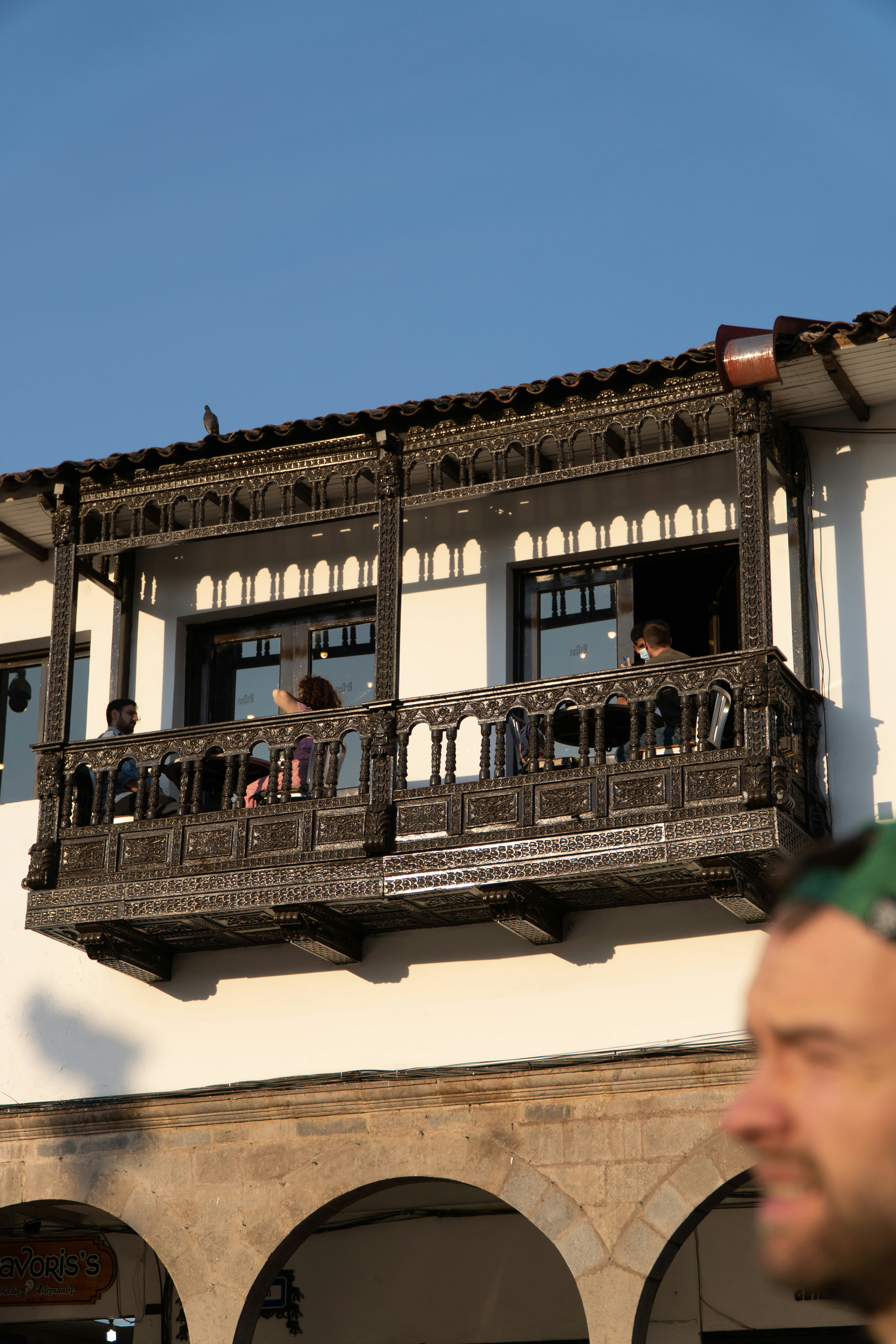 Ornate balcony on a white building with people inside.