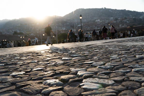 People walk on a cobblestone path at sunset.