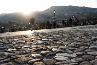 People walk on a cobblestone path at sunset.