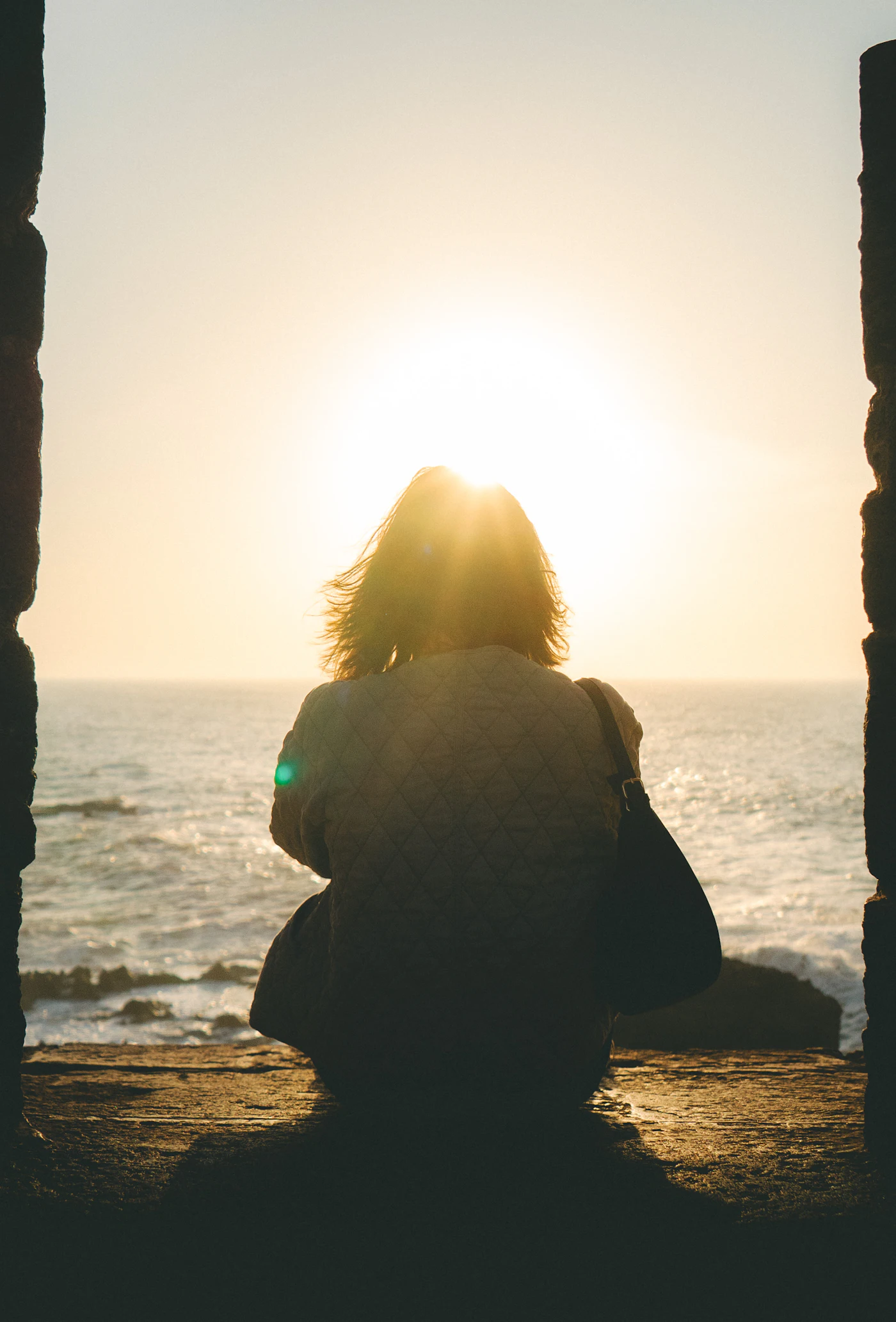 Une femme regarde le soleil se coucher sur la mer.