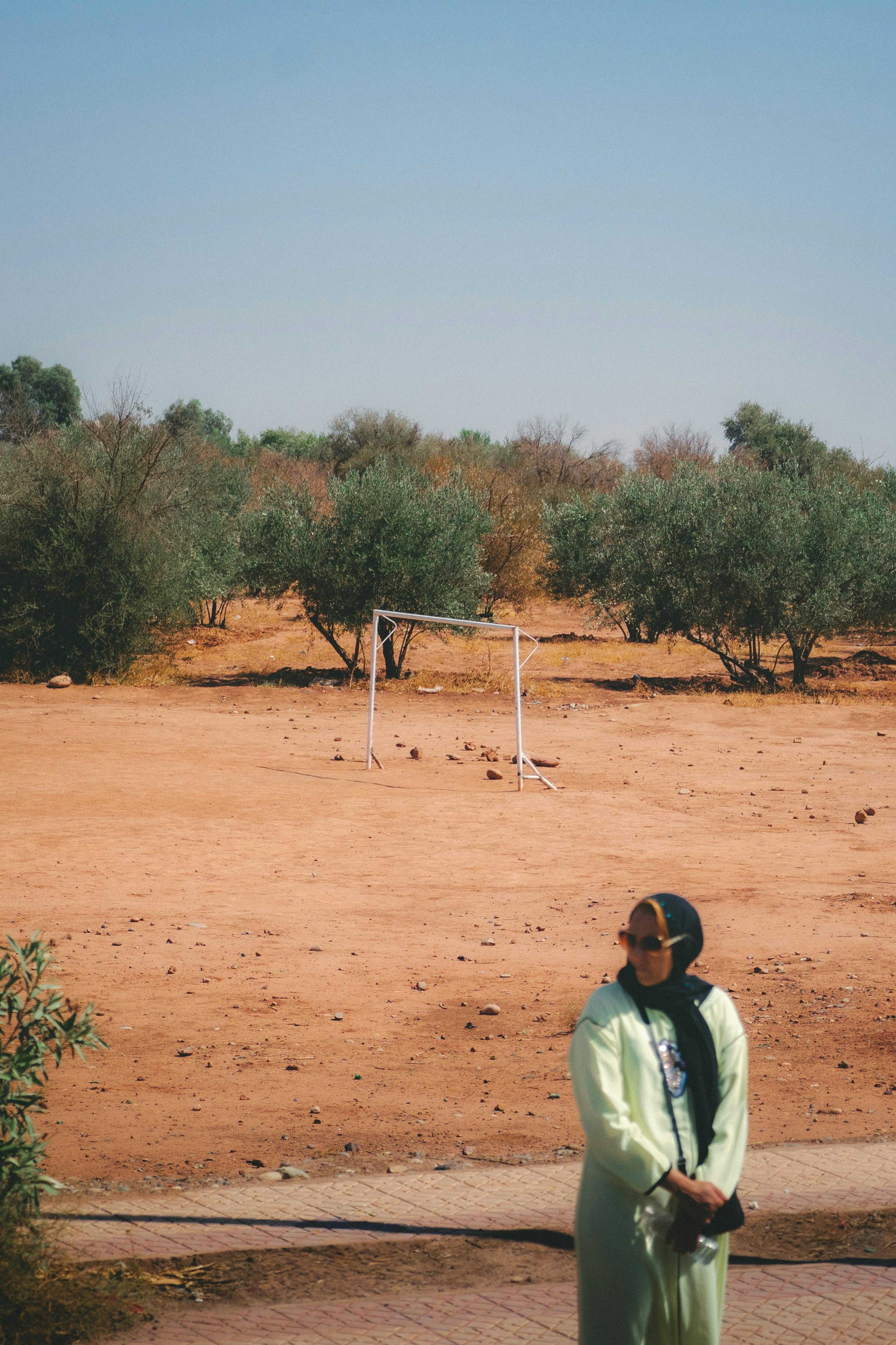 Woman in traditional dress stands in a dry, grassy field.