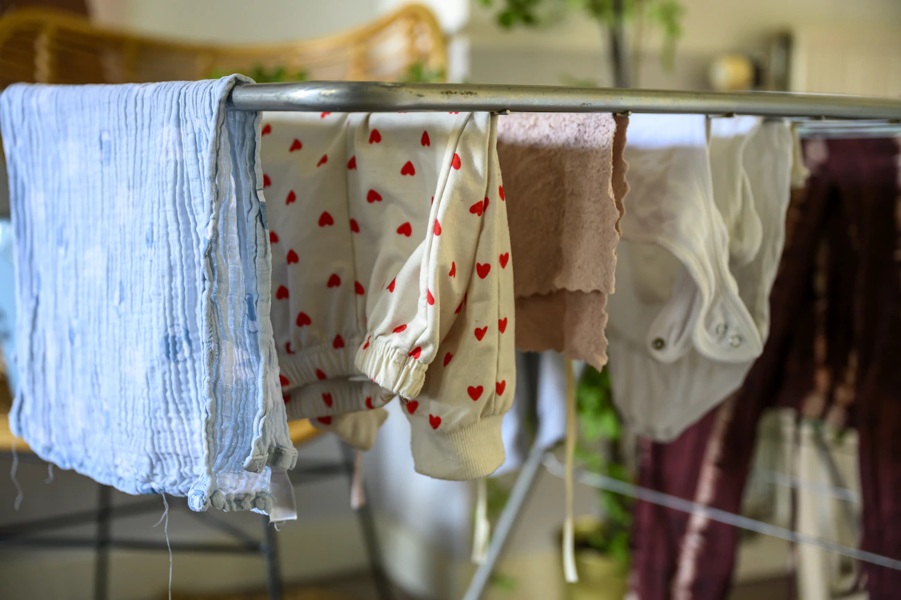 Soft baby clothes and a muslin swaddle drying on an indoor rack