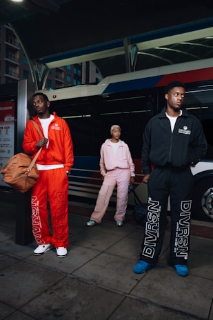 Three people in tracksuits stand near a bus.
