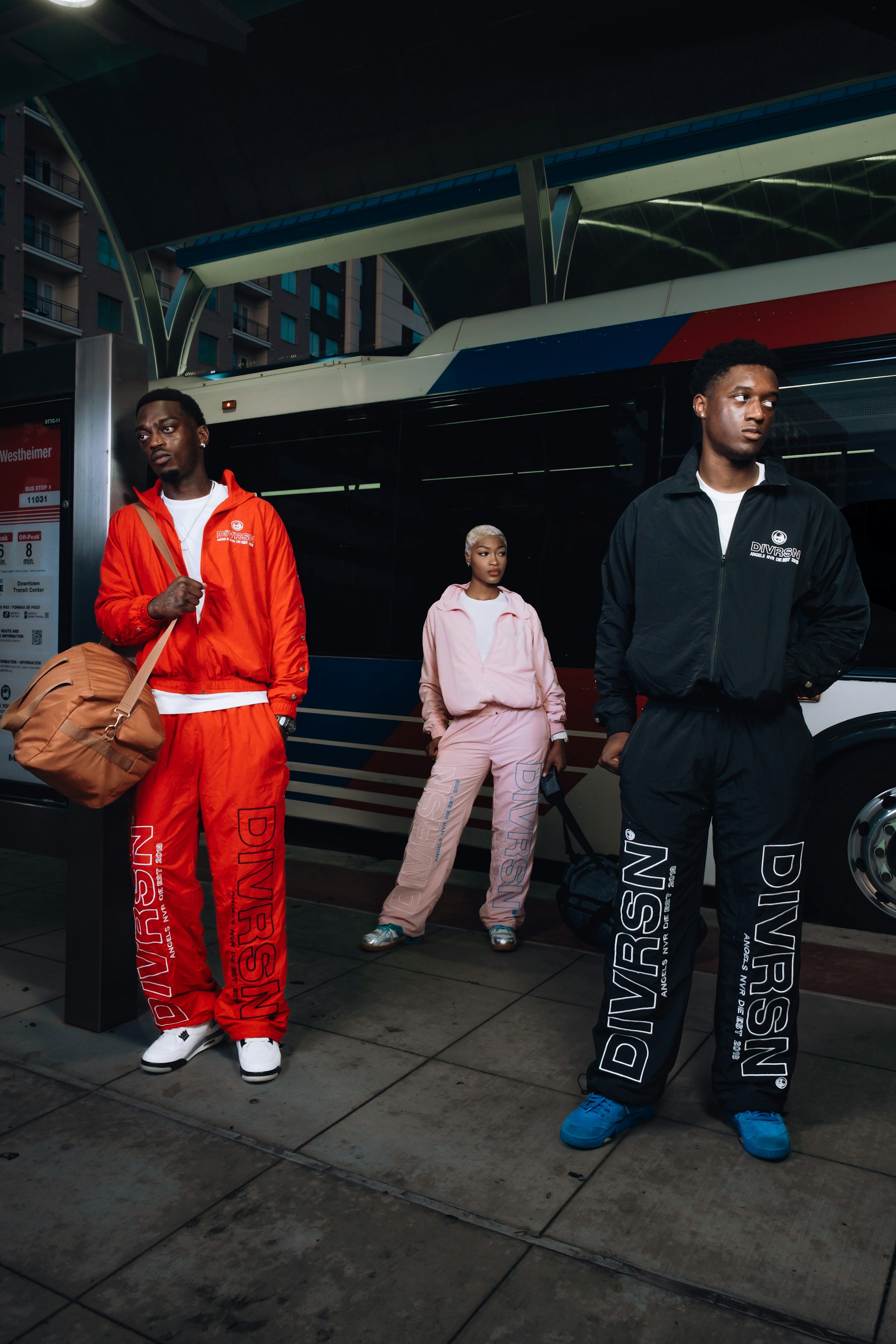 Three people in tracksuits stand near a bus.