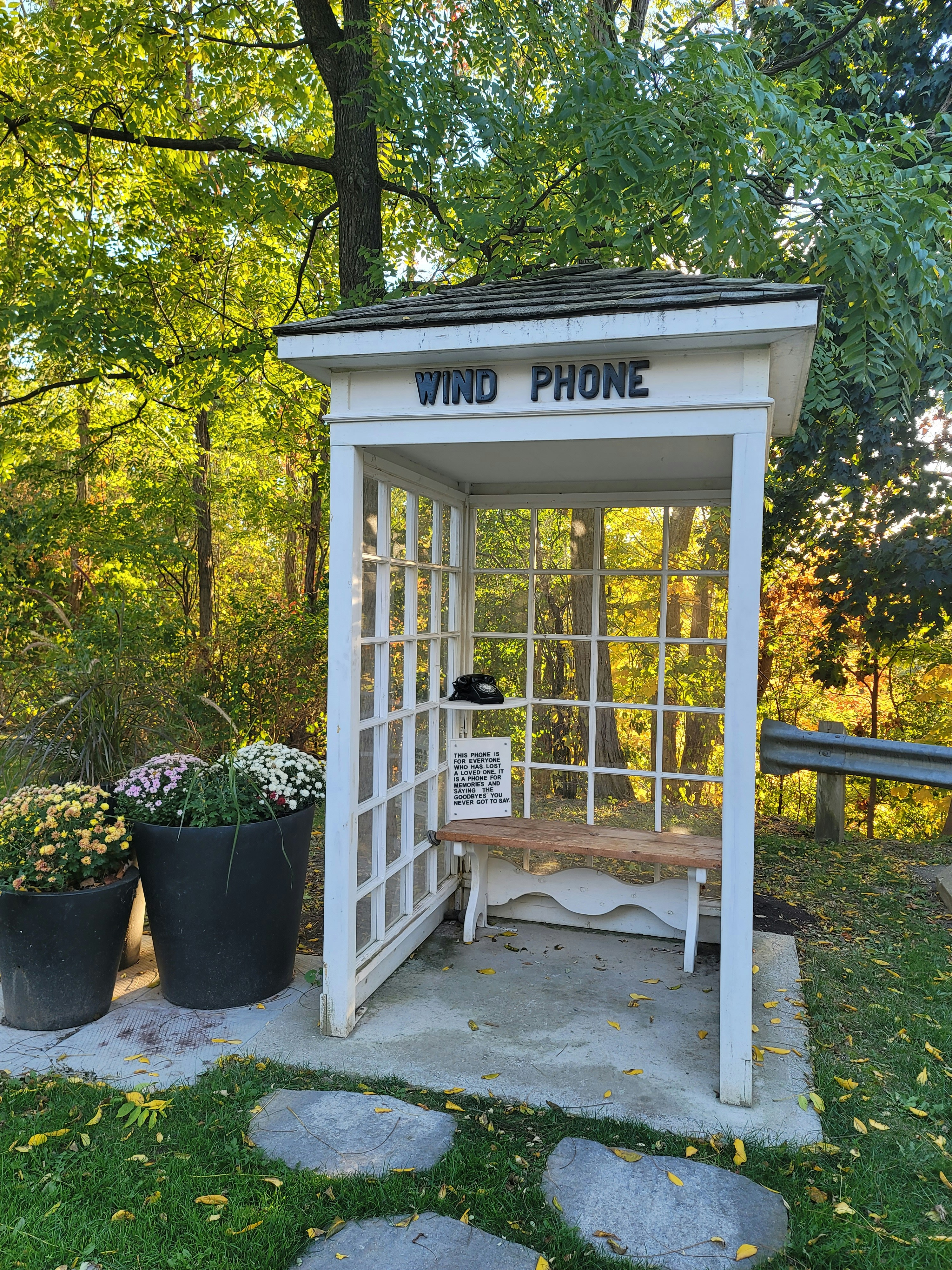 A white booth labeled "wind phone" with a bench inside.