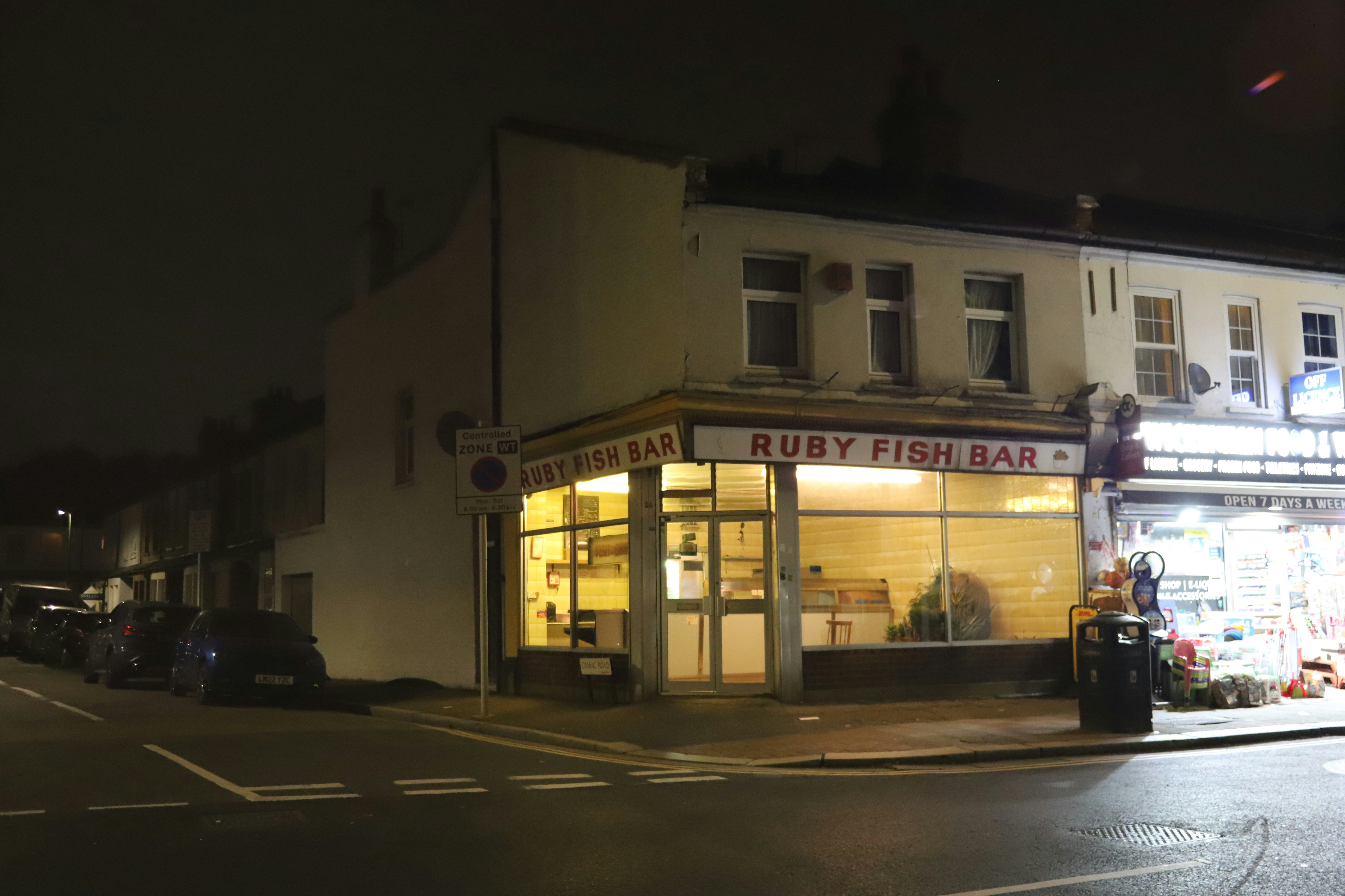 Ruby fish bar storefront at night with cars on street