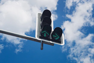 Traffic light with green arrows against blue sky