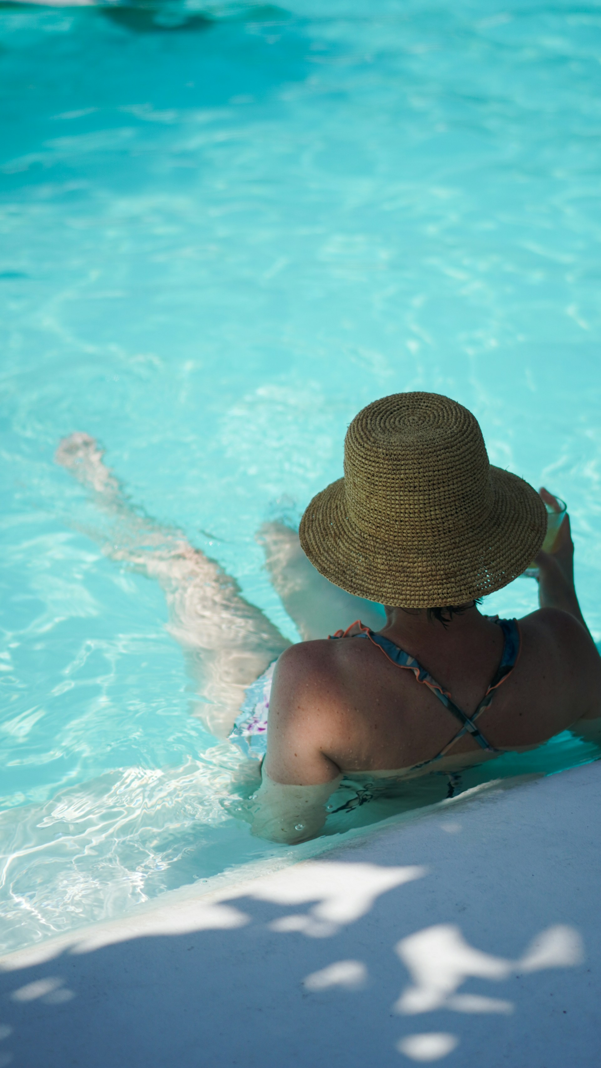 Woman in a straw hat relaxes in a swimming pool.