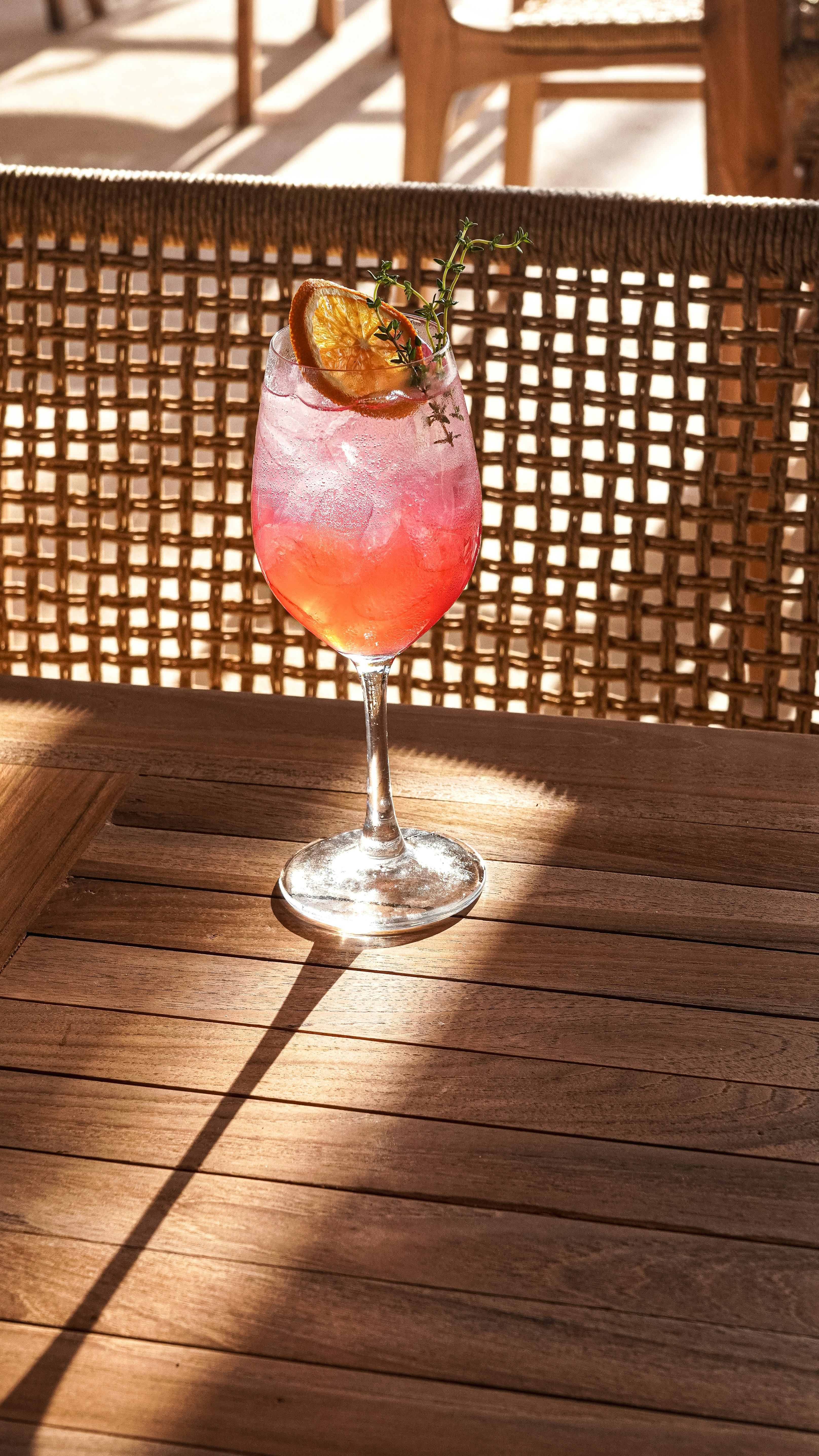 Pink cocktail with orange slice and herb garnish.