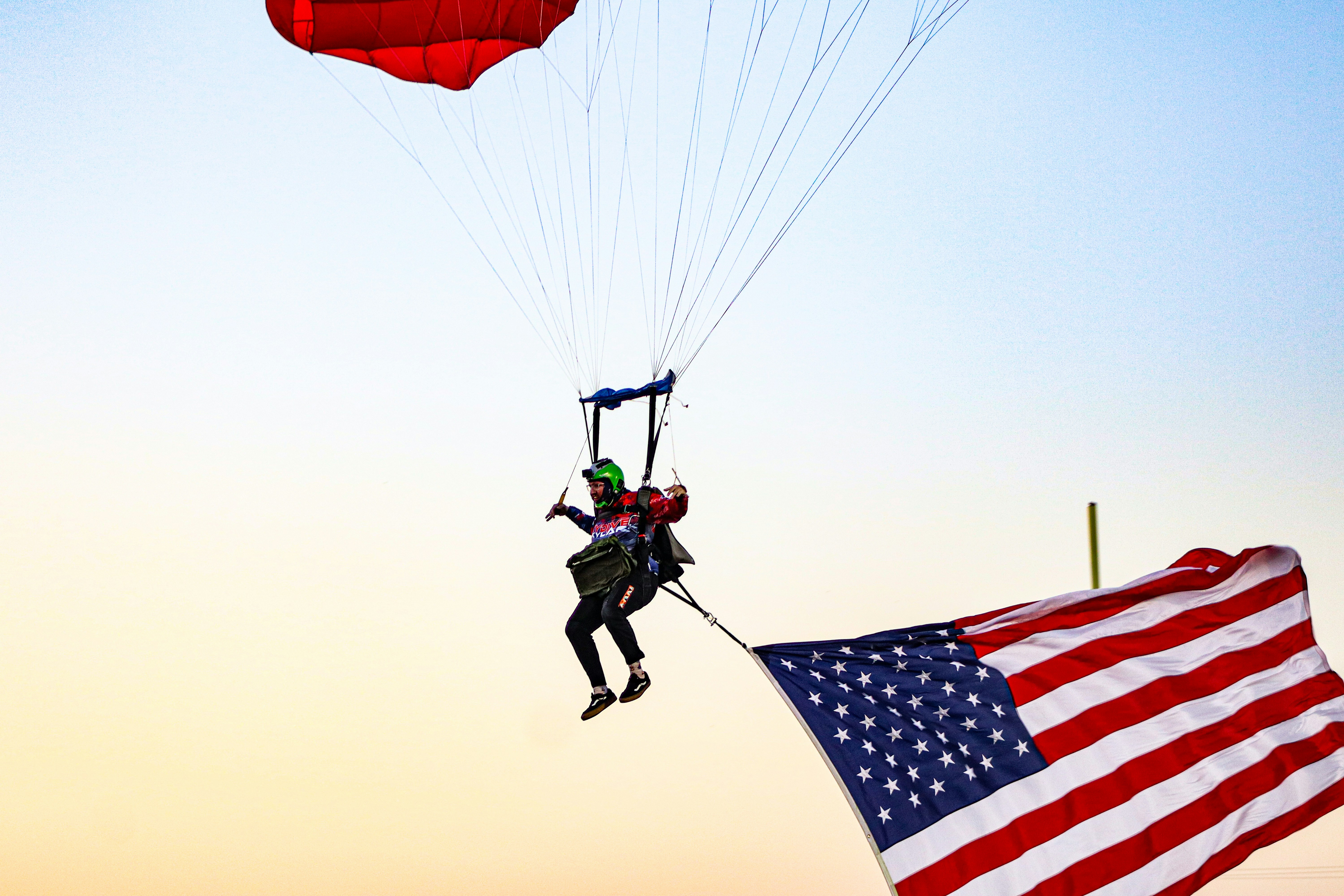 Skydiver with american flag descends against clear sky