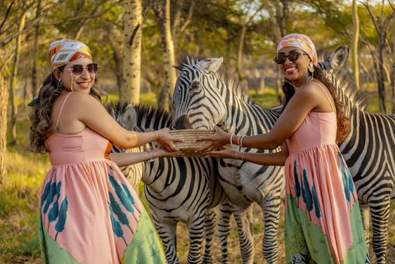 Two women in matching dresses feed zebras