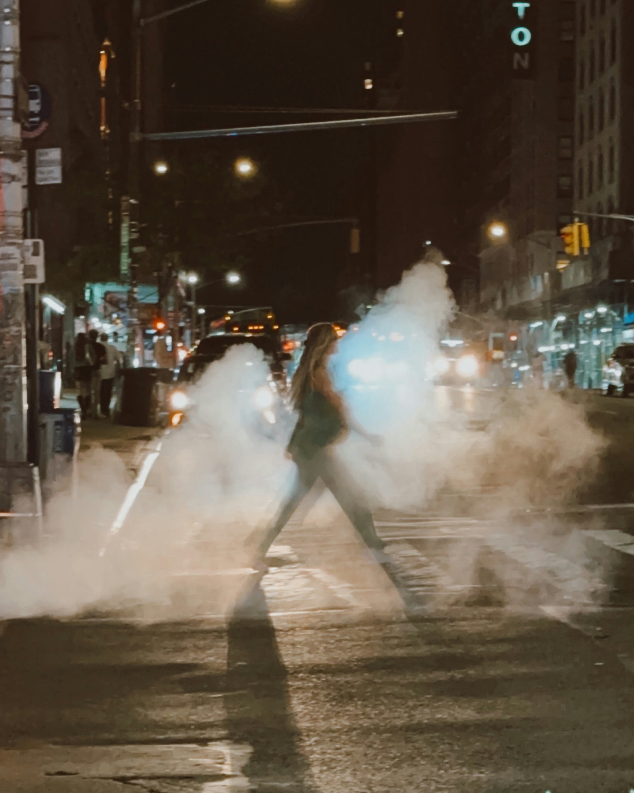 Woman walks through steam on city street at night