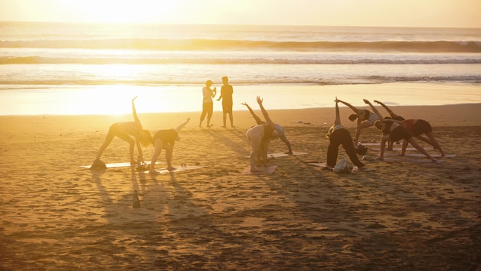 People practicing yoga on a beach at sunset.